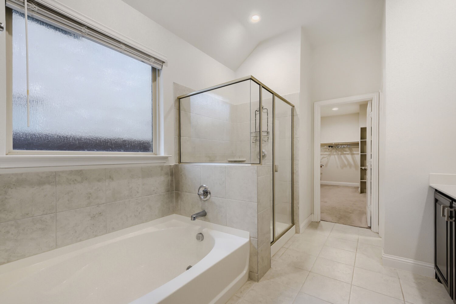 Bathroom with a soaking tub, glass-enclosed shower, and doorway to a walk-in closet.