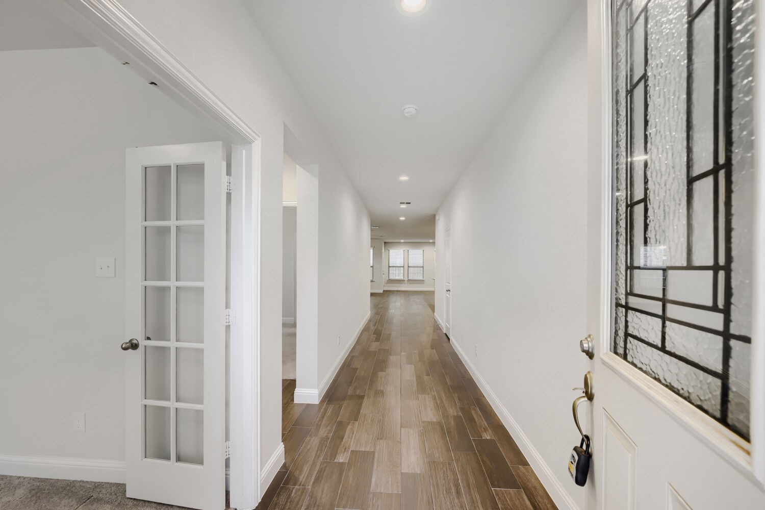 Entry hallway with wood-look tile flooring, glass-paneled doors, and windows at the far end.