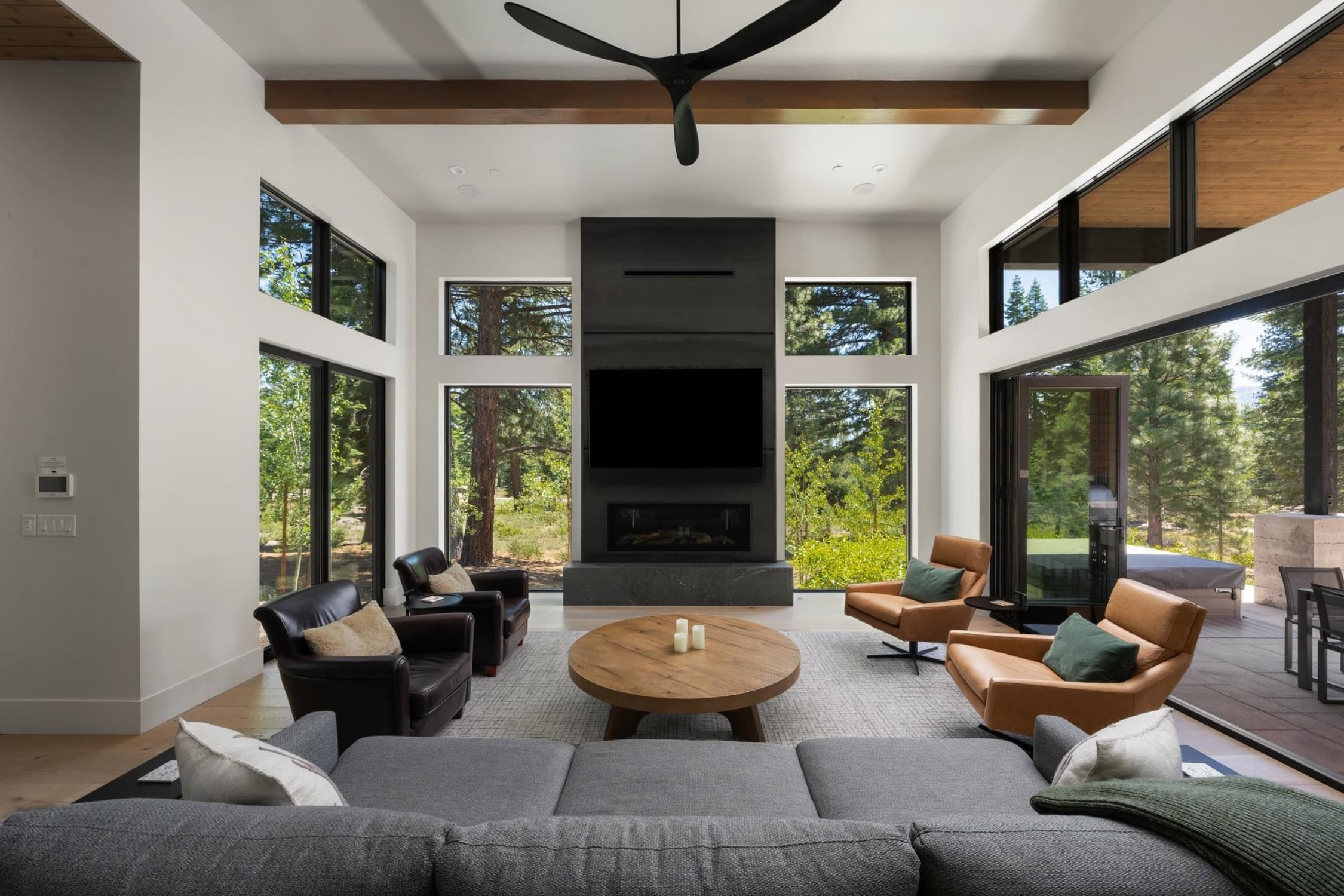 Modern living room with a tall fireplace, expansive windows, and views of pine trees.