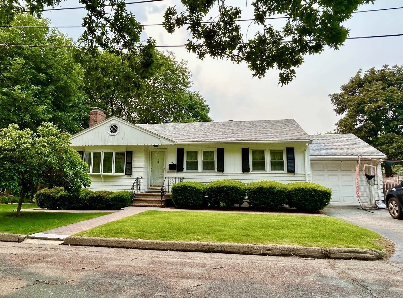 White ranch-style house with black shutters, an attached garage, and a brick walkway across the lawn.