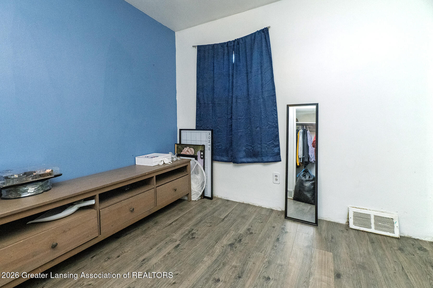Bedroom with a blue accent wall, wood-look flooring, a dresser, dark curtains, and a full-length mirror.