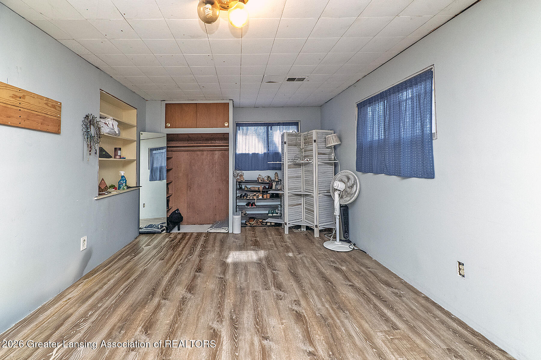 Room with built-in closet, shoe racks, blue curtains, and wood-look flooring.