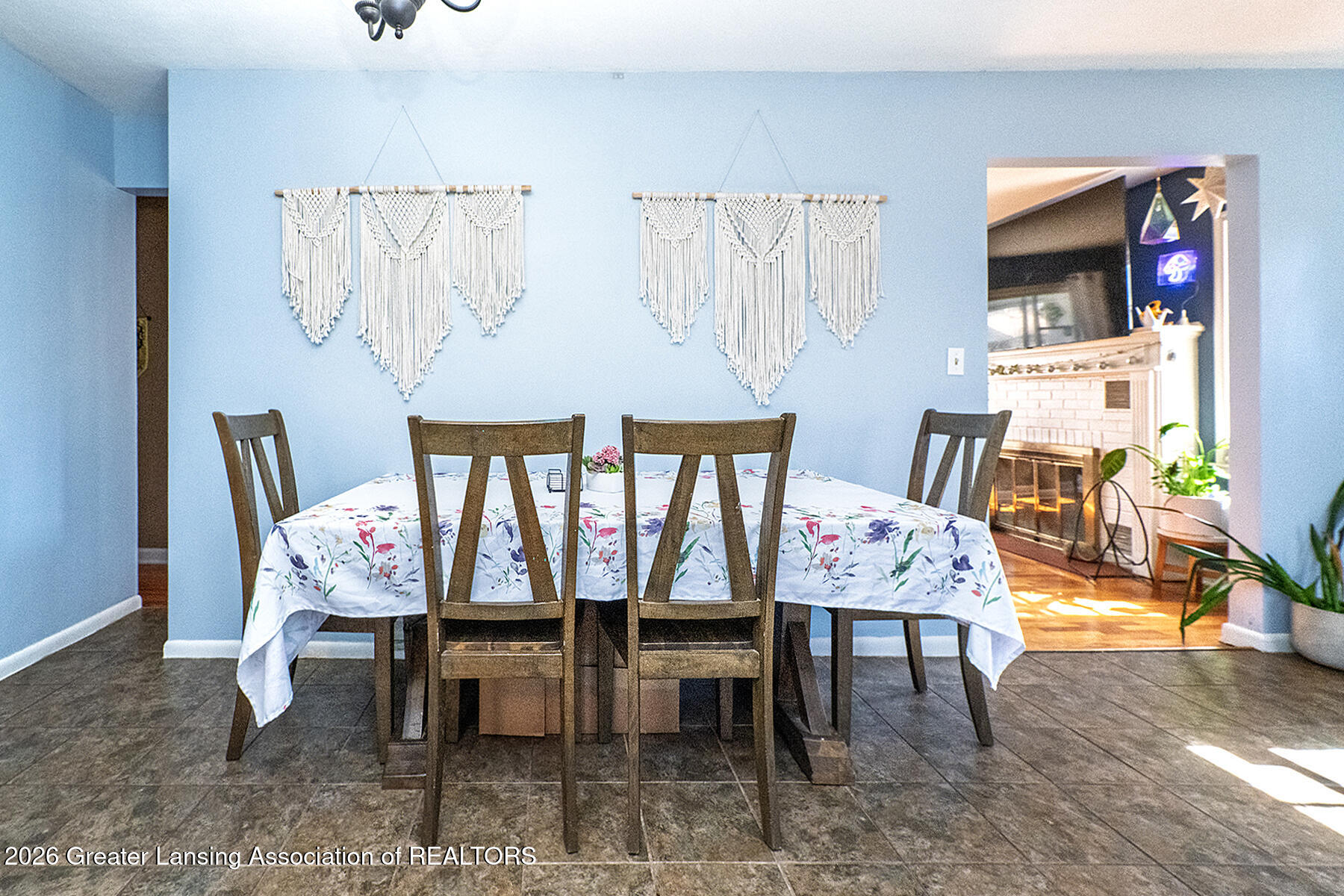 Dining room with a floral-covered table, wooden chairs, blue walls, and a doorway to a living room with a fireplace.