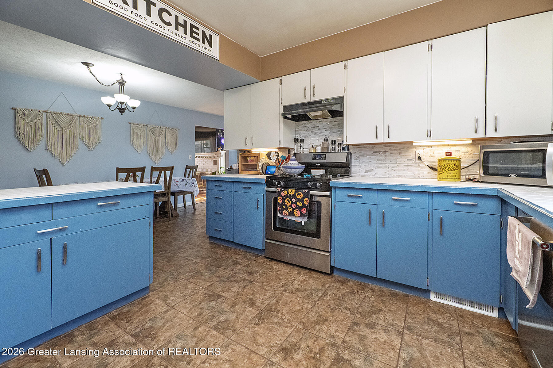 Kitchen with bright blue cabinets, white upper cabinets, and a stainless-steel range opening onto a dining area.