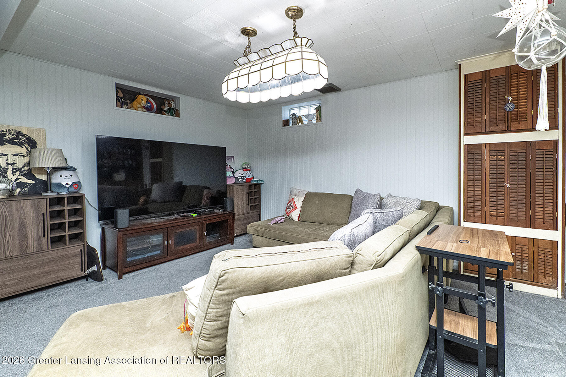 Living room with a large sectional sofa, television, blue-gray carpet, and tall wooden louvered doors.
