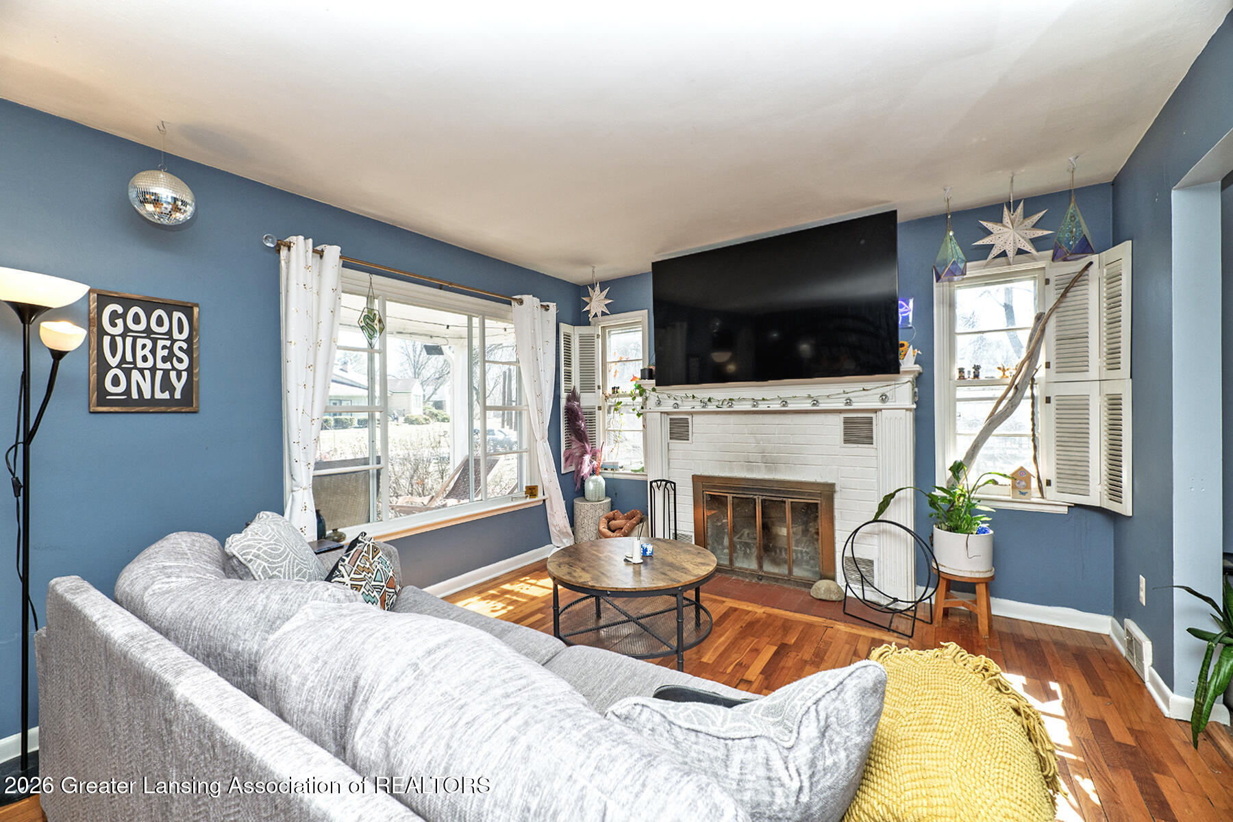 Living room with a white brick fireplace, oversized television, blue walls, and hardwood floors.