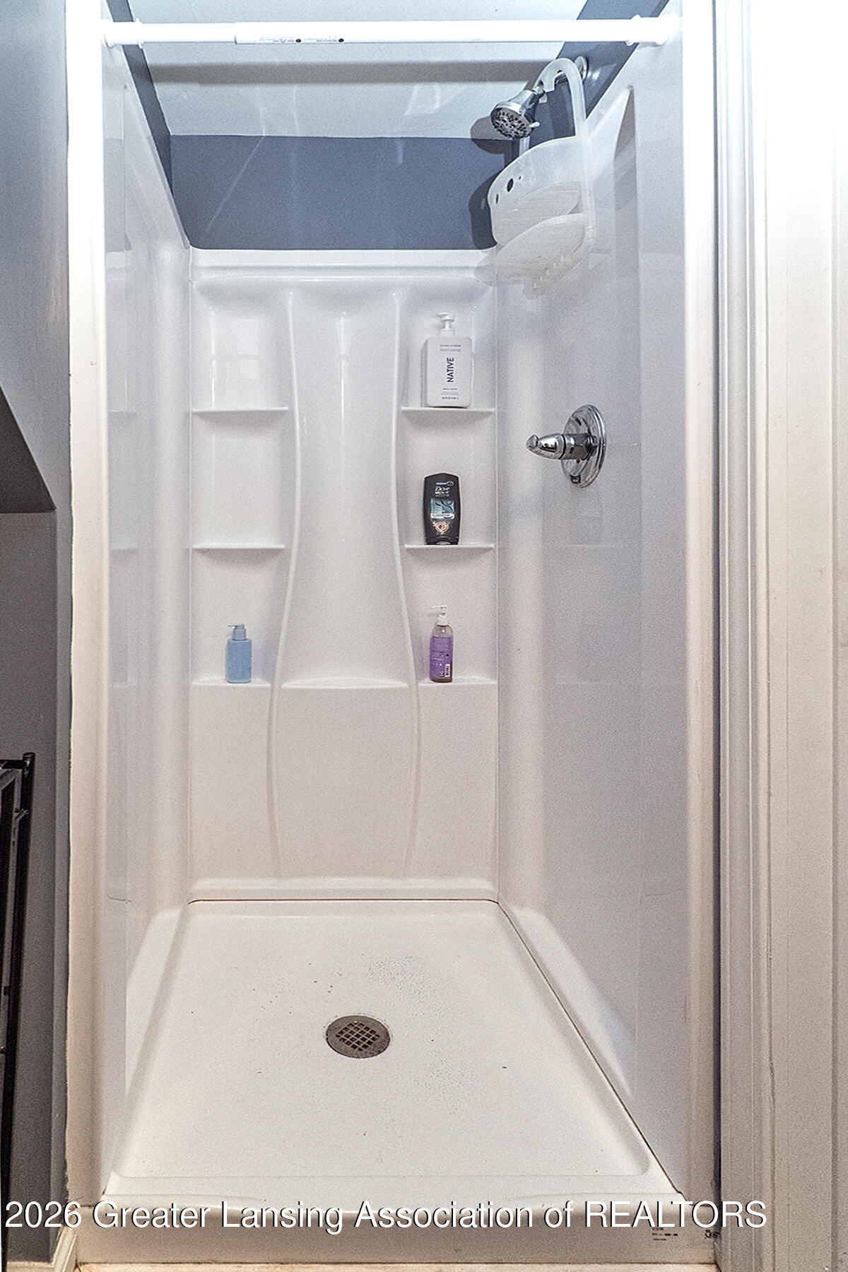 White walk-in shower with a handheld showerhead, chrome controls, and built-in toiletry shelves.