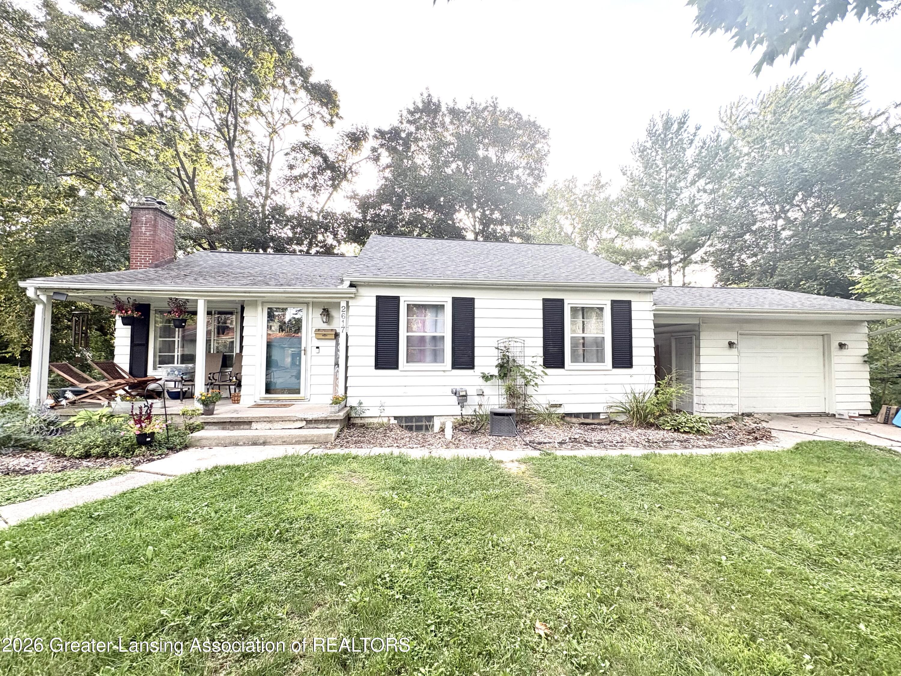 White single-story home with black shutters, a covered porch, and an attached garage.