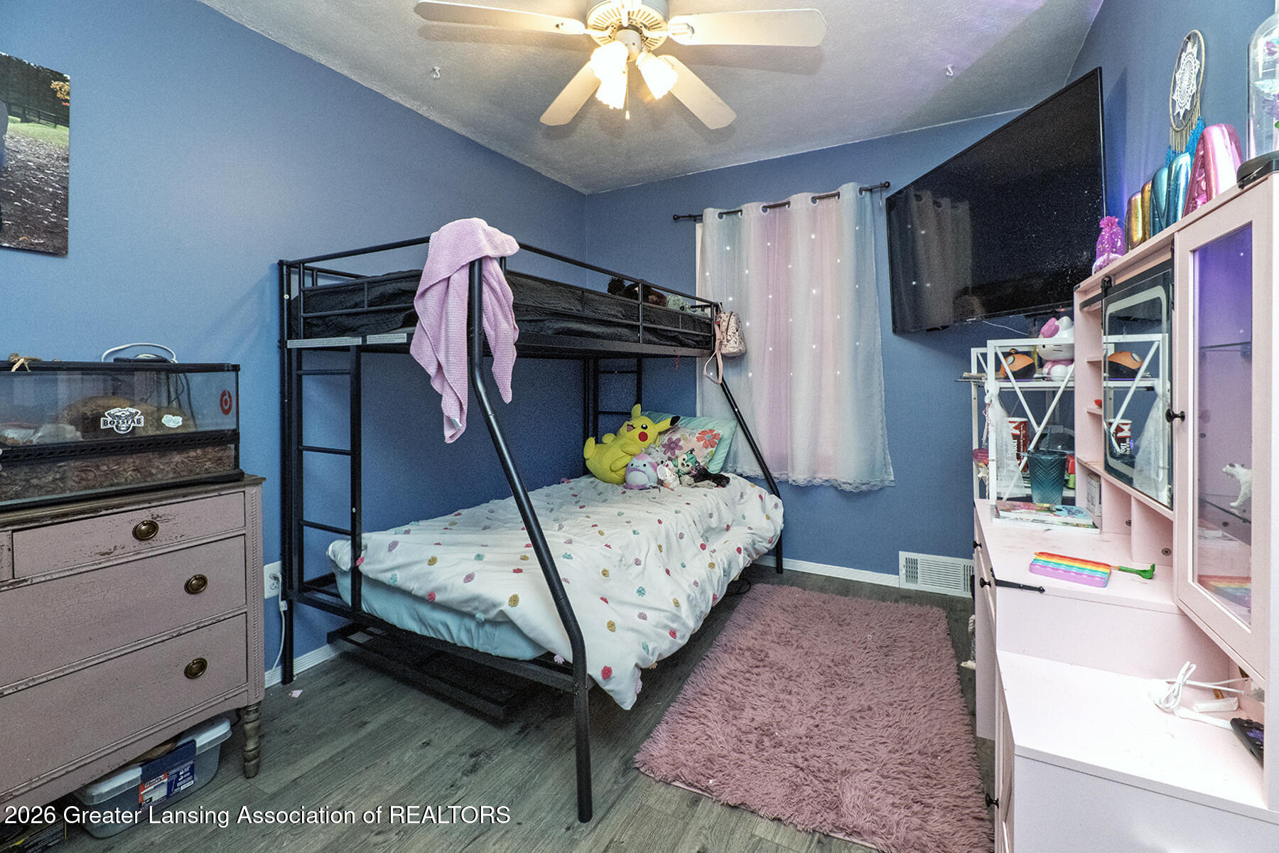 Blue bedroom with a black metal bunk bed, pink cabinet, wall-mounted television, and mauve rug.