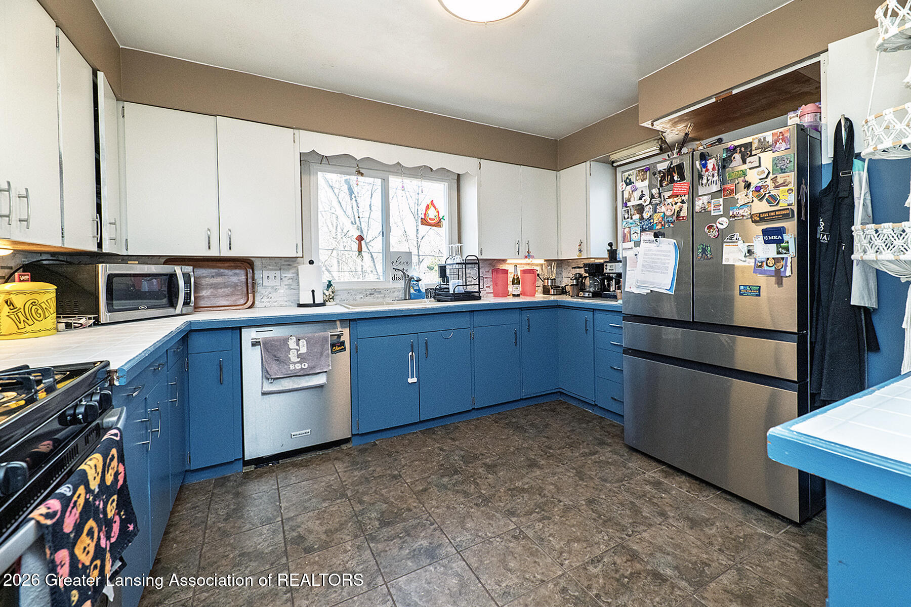 Kitchen with blue cabinets, white upper cupboards, and a magnet-covered stainless steel refrigerator.