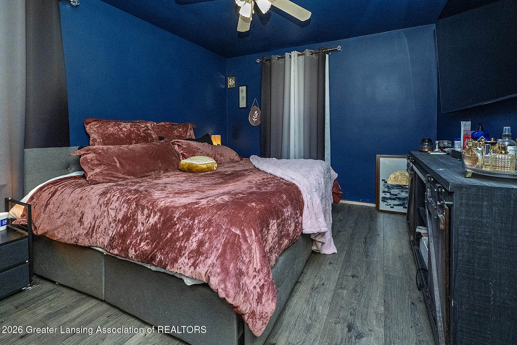 Bedroom with deep blue walls, rose-colored bedding, and gray wood-look floors.