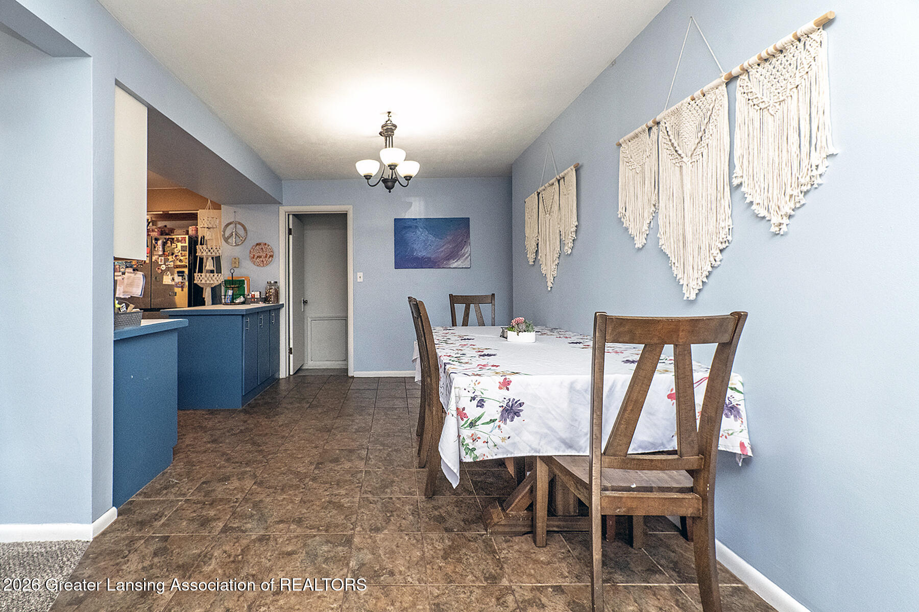Dining room with a wooden table, floral tablecloth, woven wall hangings, and blue kitchen counter.