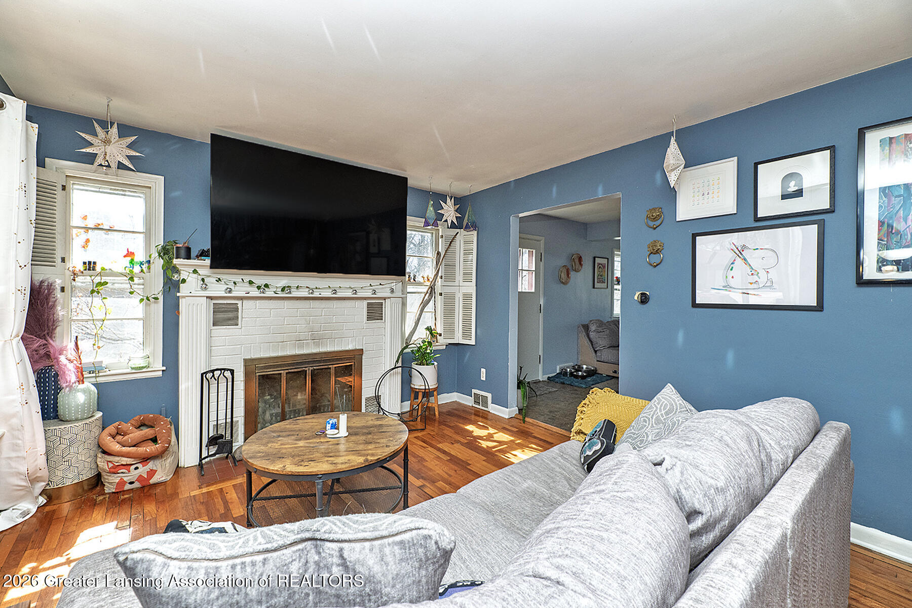 Living room with a white brick fireplace, blue walls, hardwood floors, and gray sectional sofa.