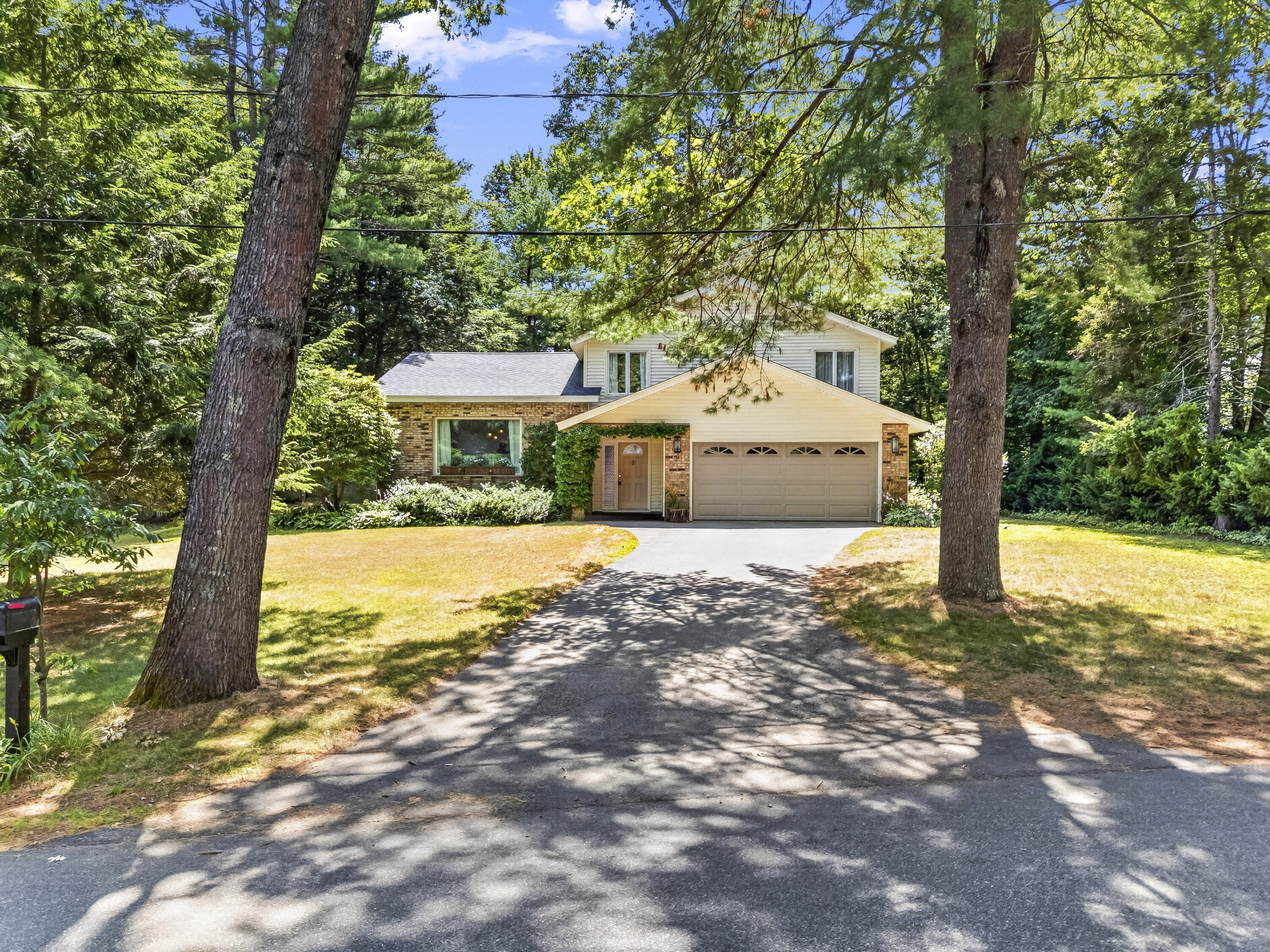 Two-story brick and siding house with a two-car garage, shaded by mature trees.