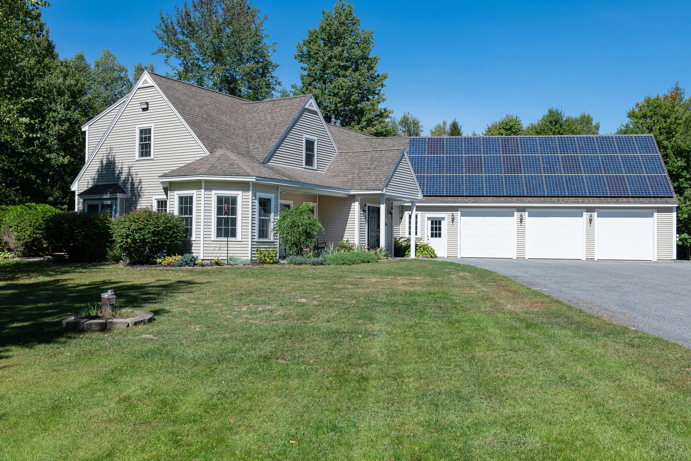 Light-colored gabled house with rooftop solar panels over a three-car garage and a broad front lawn.