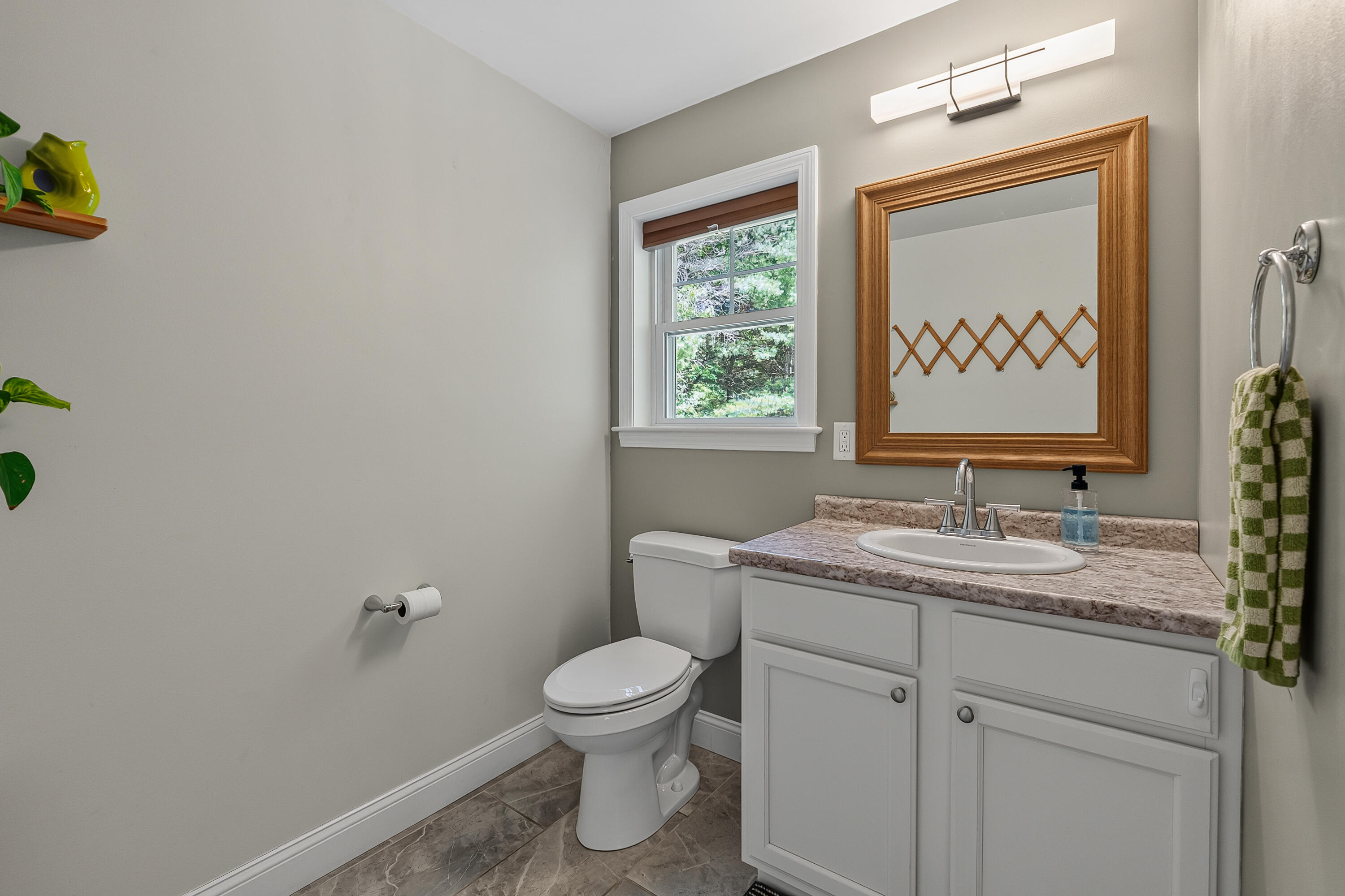 Bathroom with a white vanity, marbled countertop, wood-framed mirror, and window.