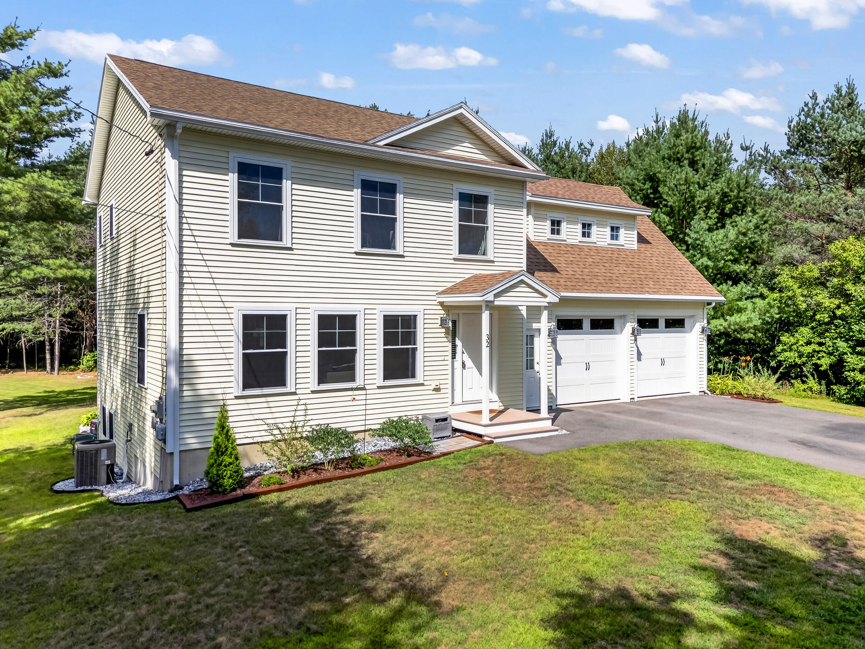 Two-story light-sided house with a covered entry porch and attached two-car garage, surrounded by trees.
