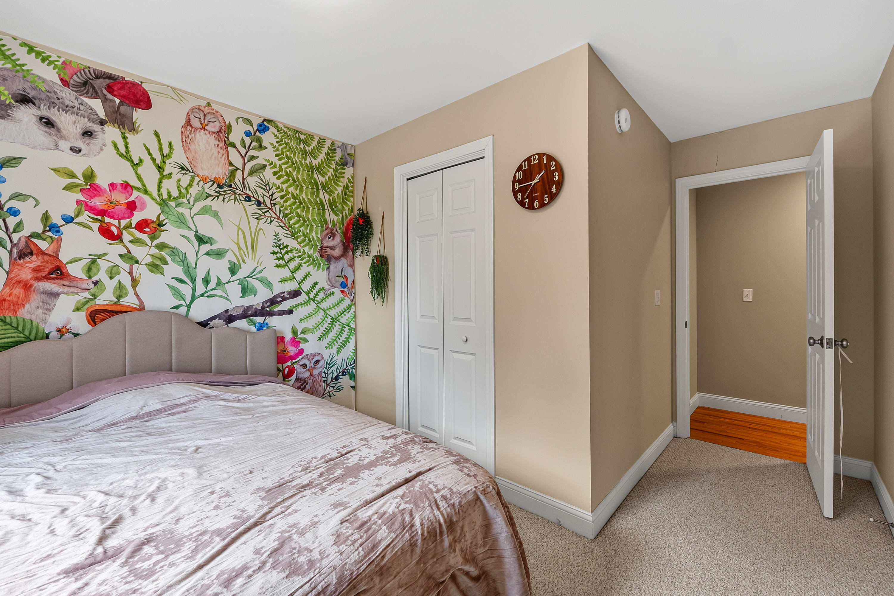 Bedroom with a bed beneath a colorful woodland-animal mural and an open doorway to the hall.