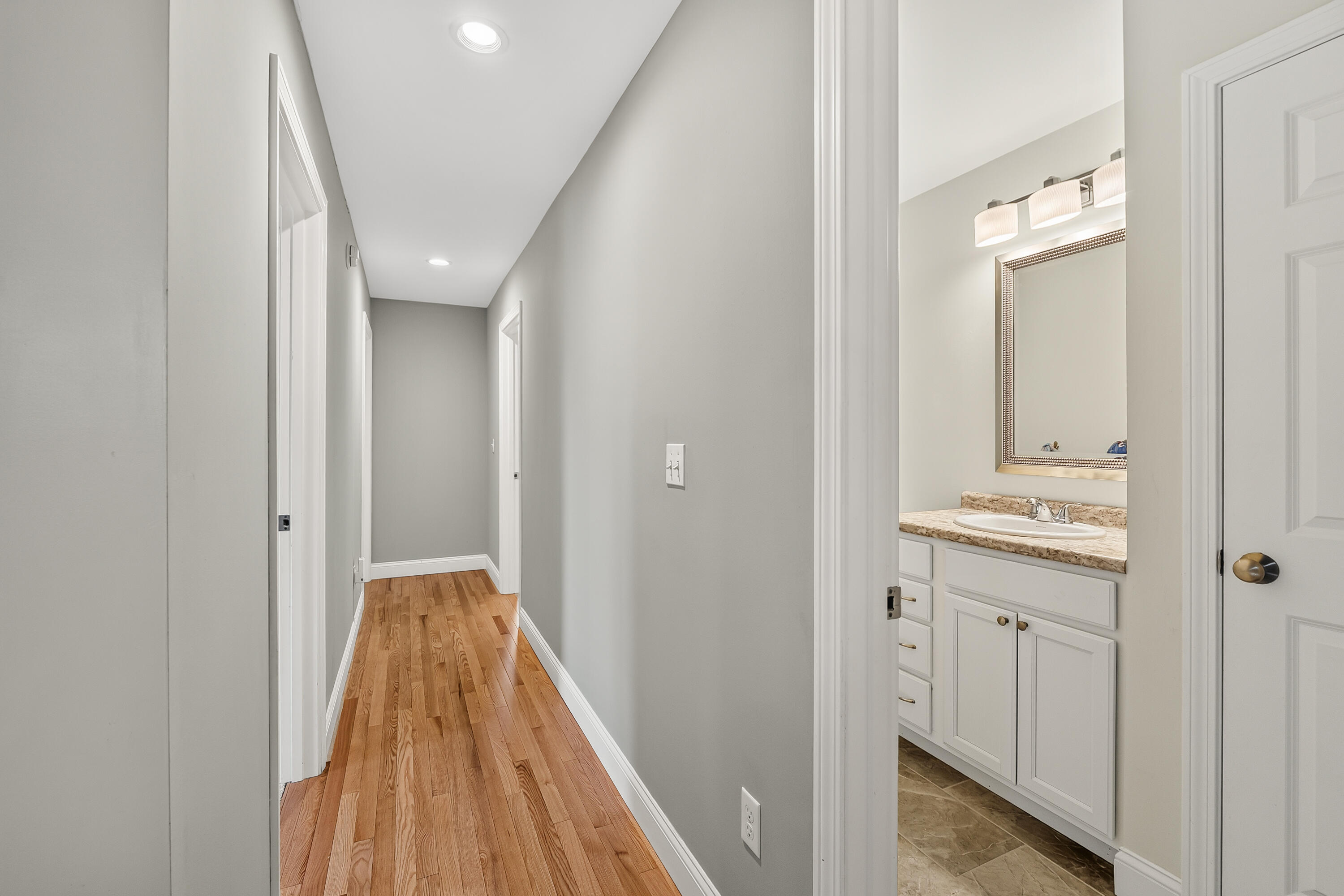 Hallway with hardwood floors and an open doorway to a bathroom vanity.