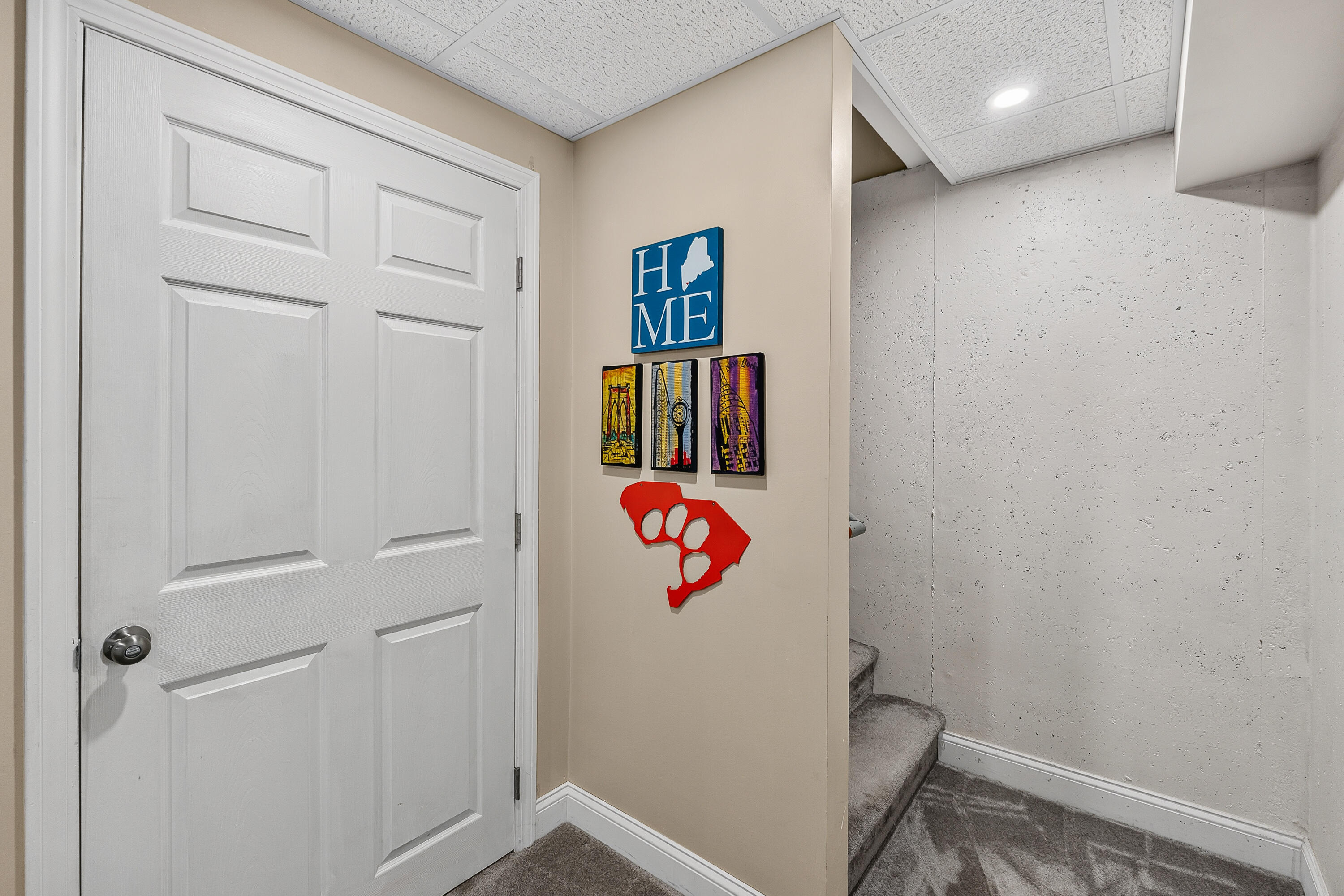 Basement stair landing with a white paneled door, carpeted stairs, and colorful wall art.