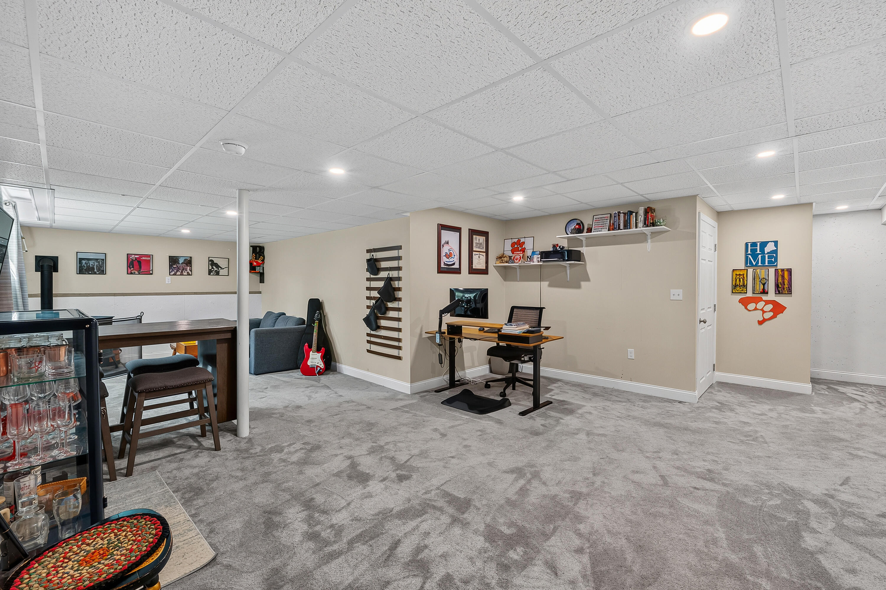 Basement recreation room with a desk, red electric guitar, game table, and glass-front beverage cooler.