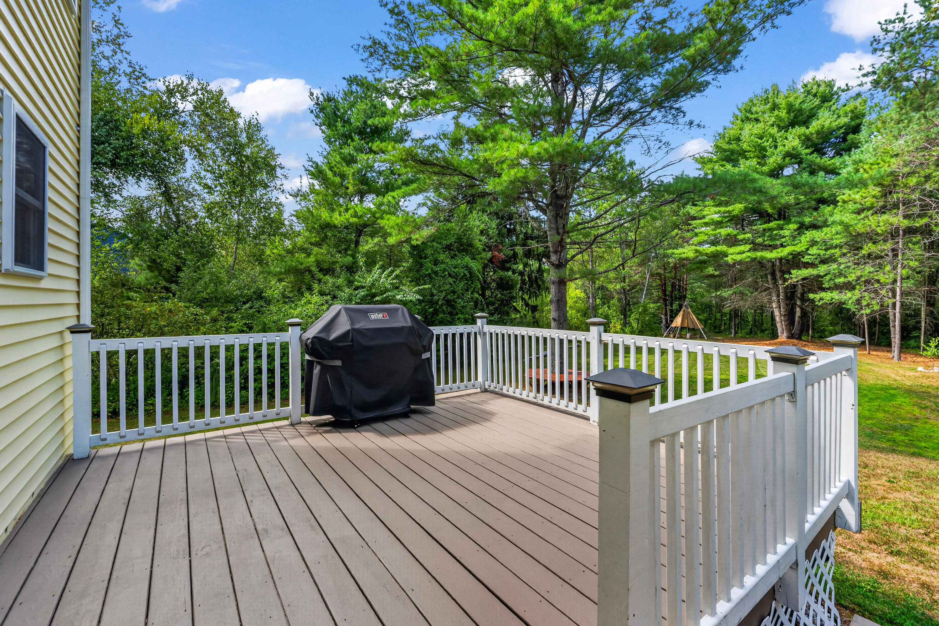 Raised gray deck with white railings and a covered grill, overlooking a wooded backyard.