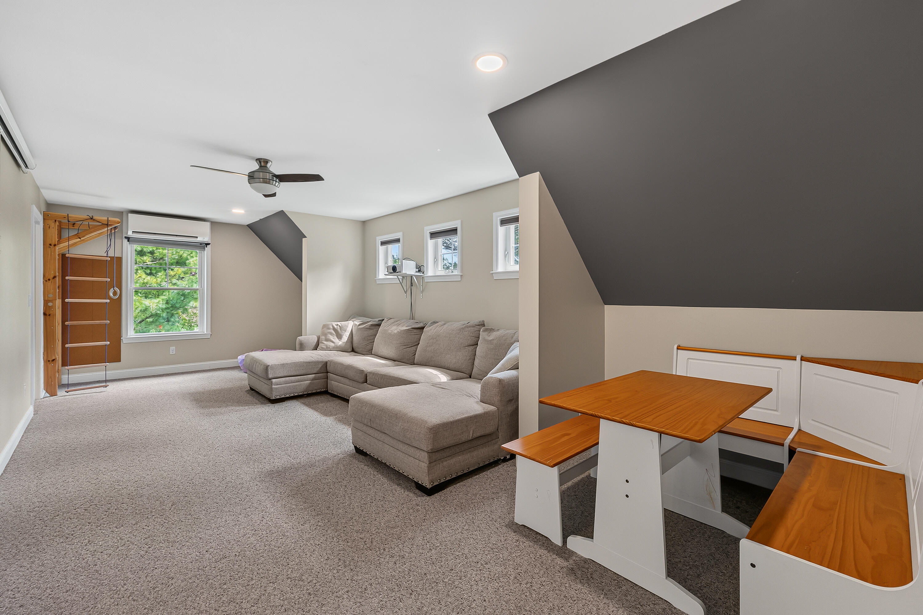 Attic living area with a gray sectional, exercise ladder, and built-in wooden table and benches.