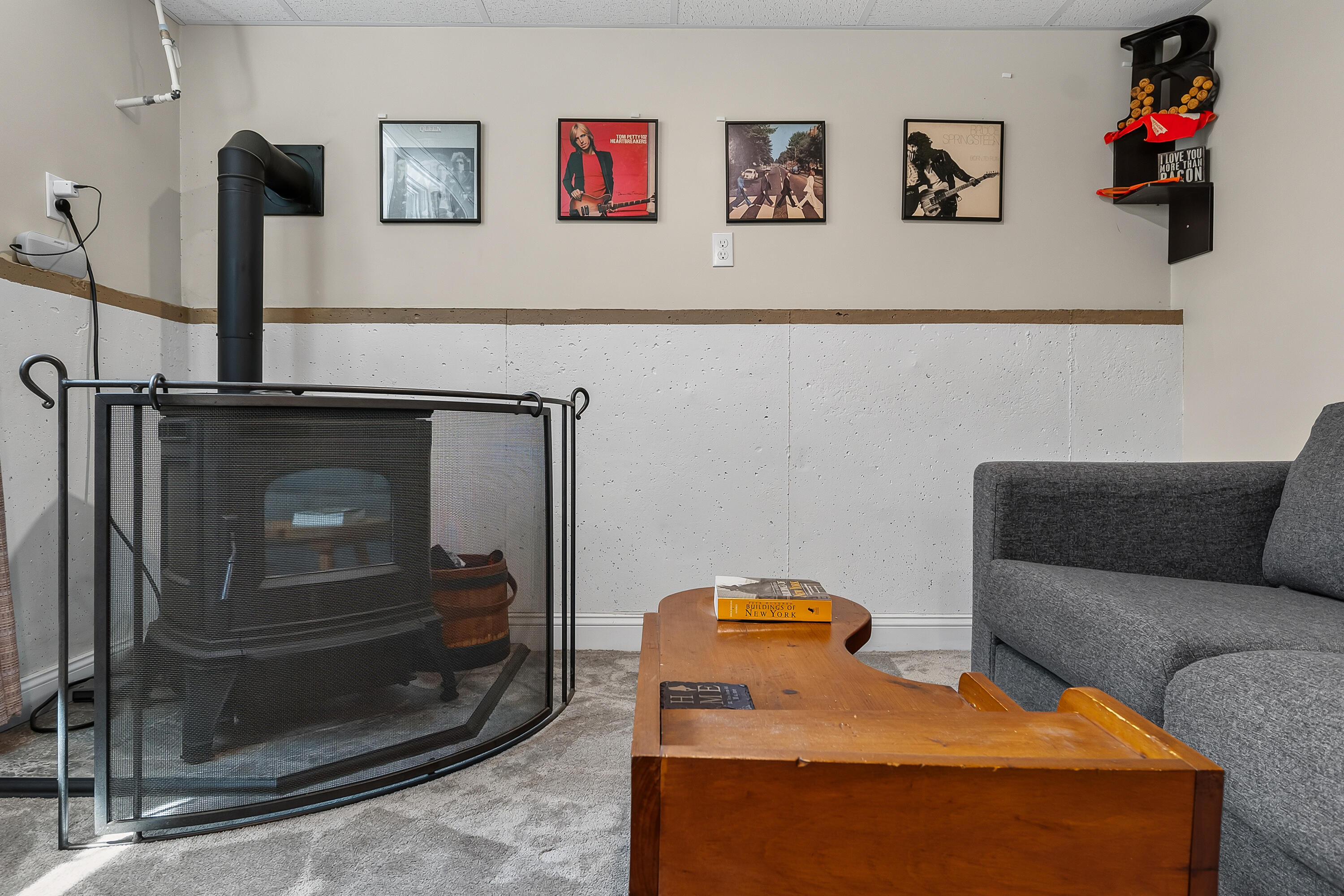 Furnished living area with a wood-burning stove, curved safety screen, gray seating, and wooden coffee table.