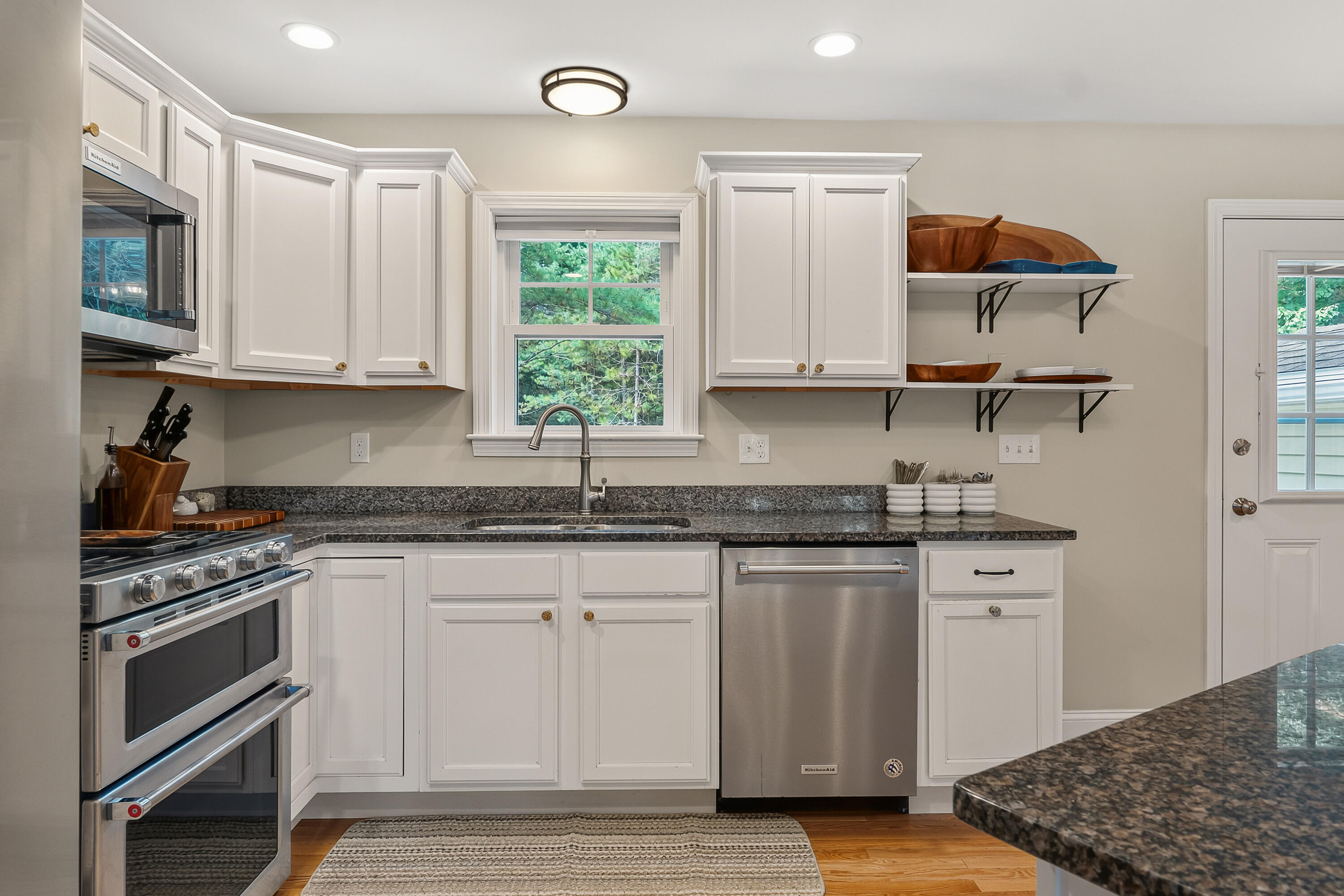 Kitchen with white cabinets, dark granite counters, stainless appliances, and a window overlooking trees.