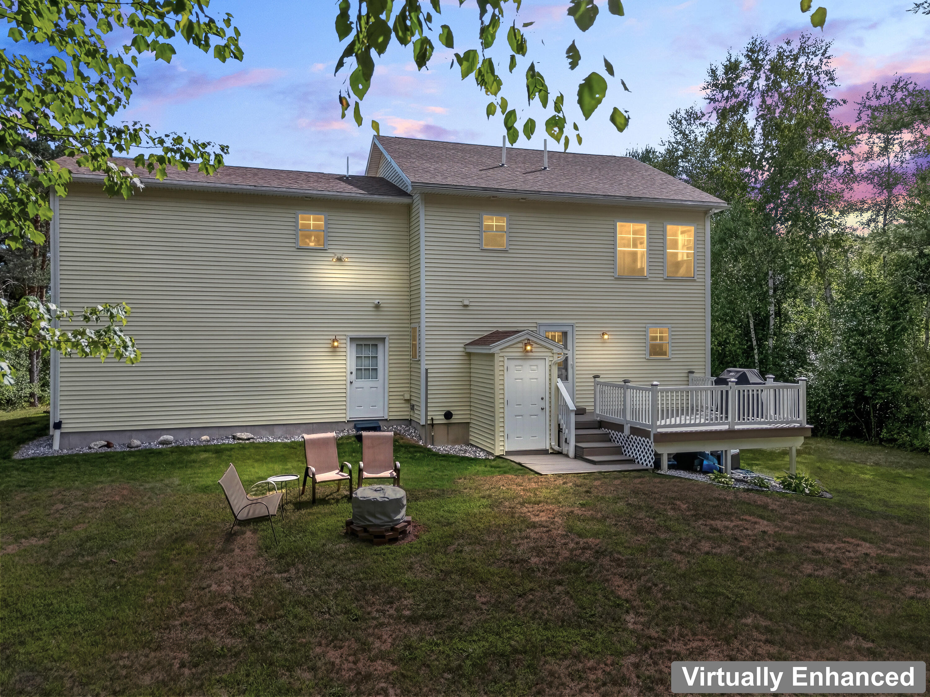 Rear of a two-story beige house with a raised deck and lawn seating at dusk.