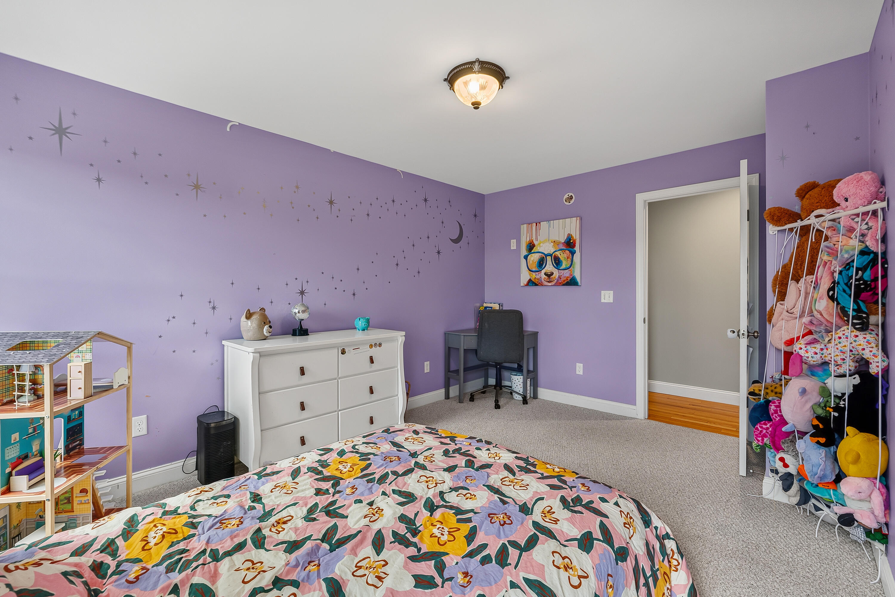 Lavender bedroom with star decals, a floral bedspread, a dollhouse, and stuffed animals on shelves.