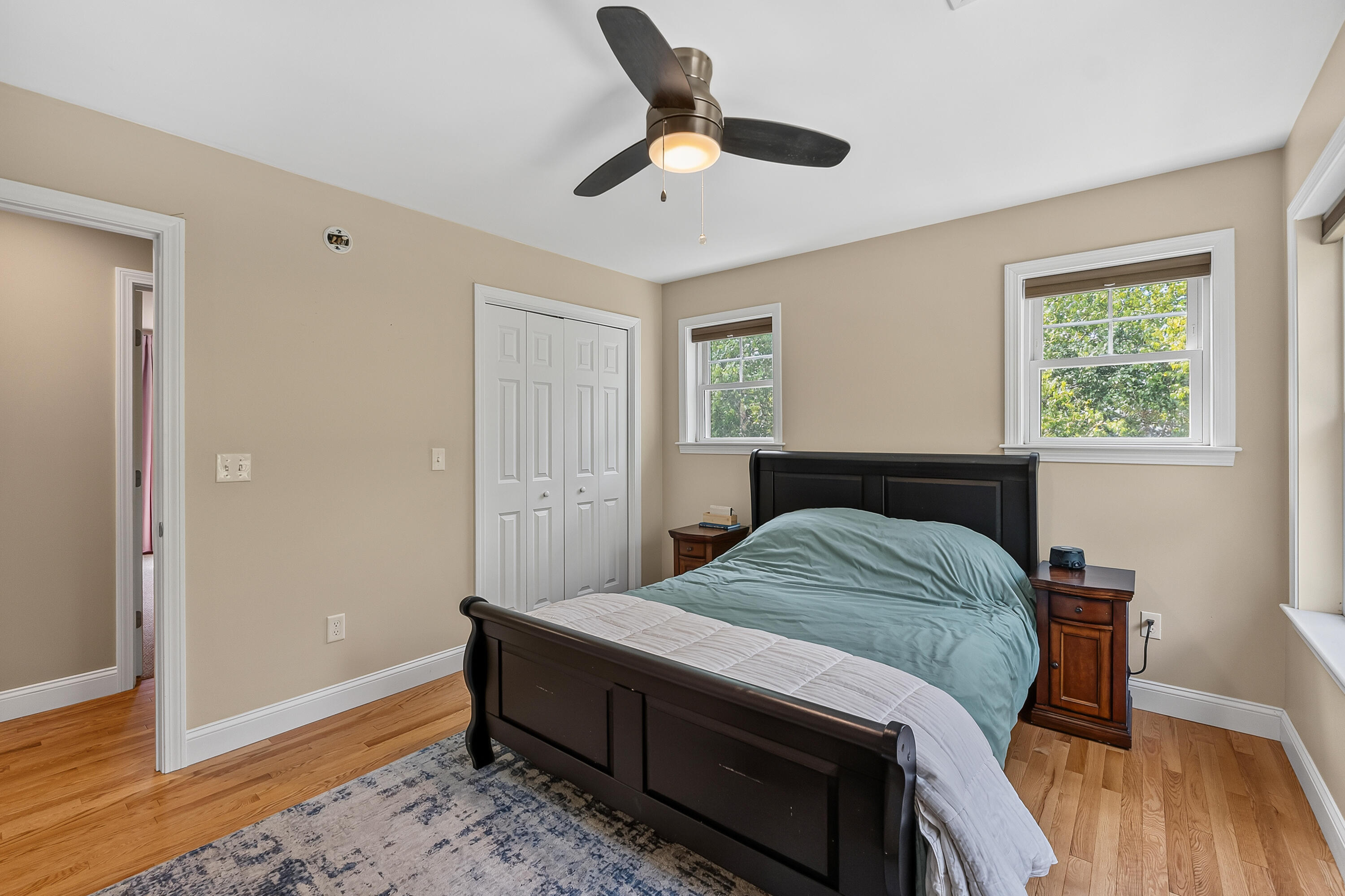 Furnished bedroom with teal bedding, a dark wood bed, hardwood floors, and two windows.