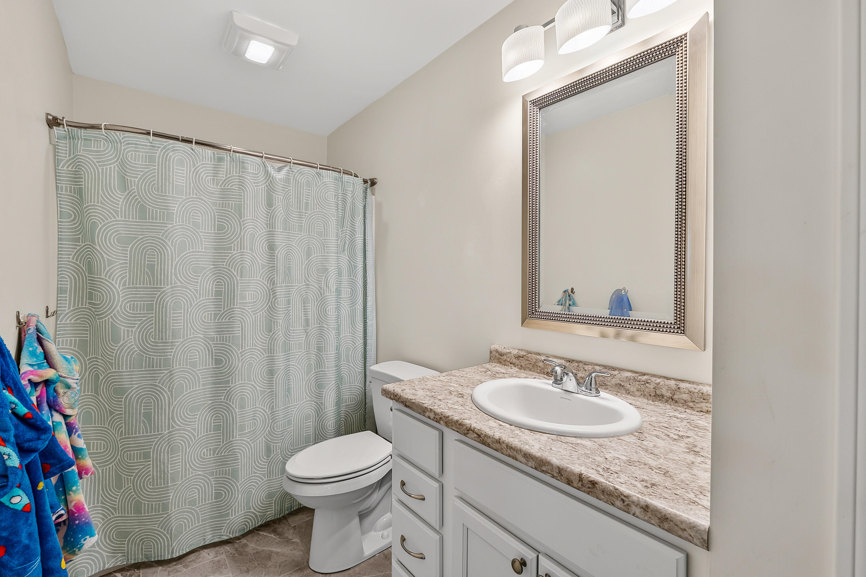 Bathroom with a gray geometric shower curtain, white vanity, and large framed mirror.