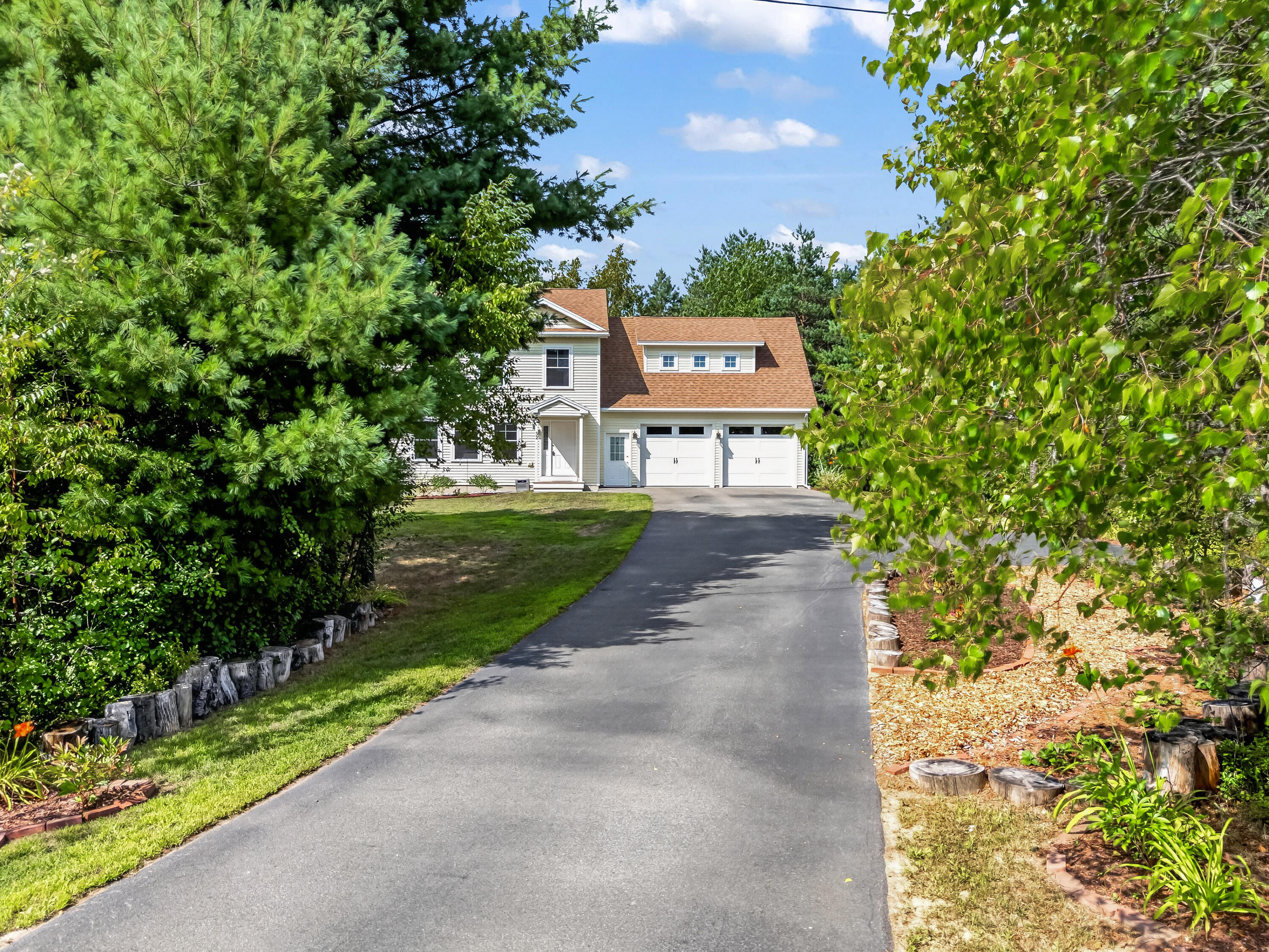 Two-story house with a two-car garage at the end of a tree-lined driveway.