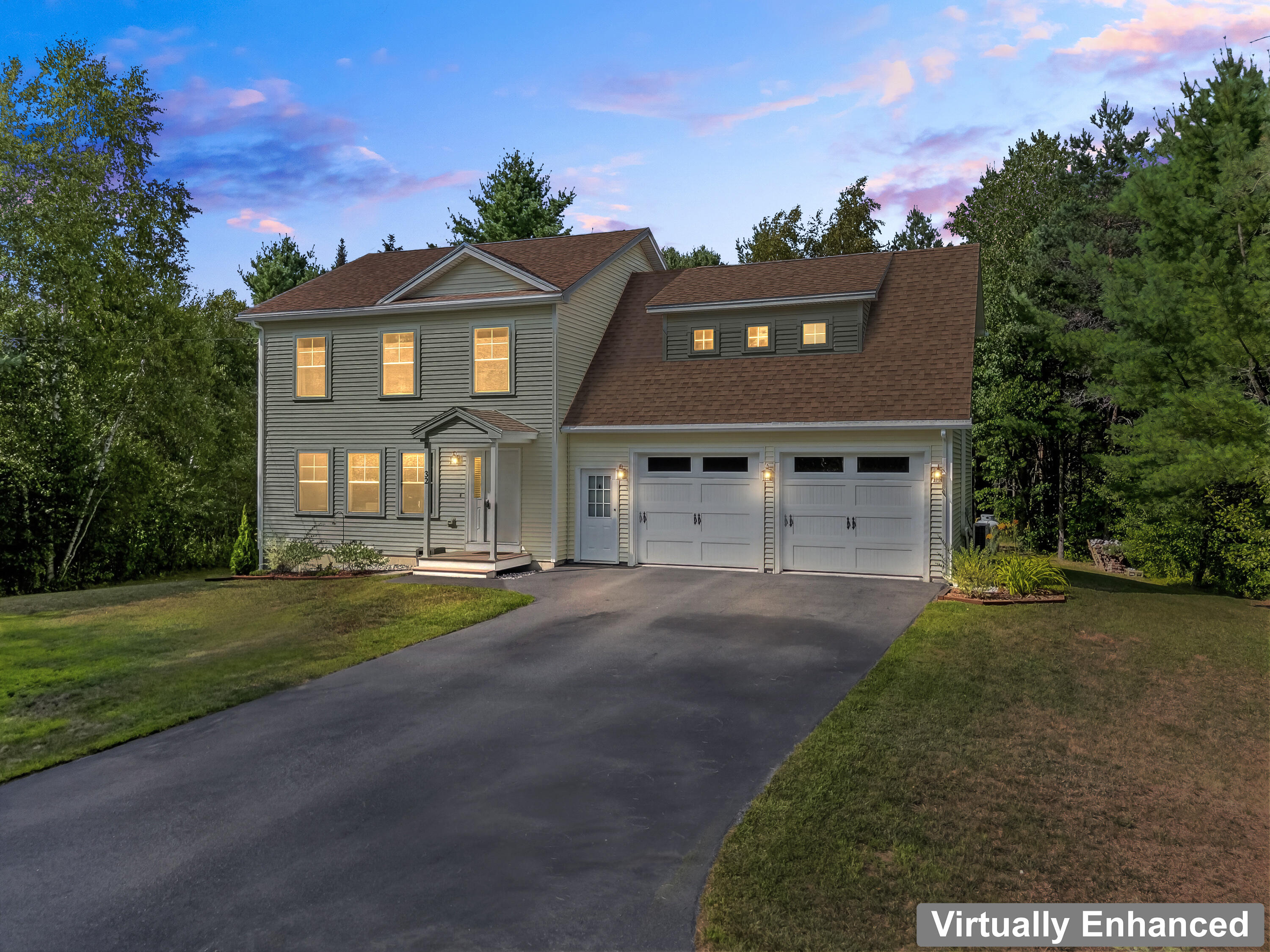 Two-story gray house with lit windows, a covered entry, and an attached two-car garage at dusk.
