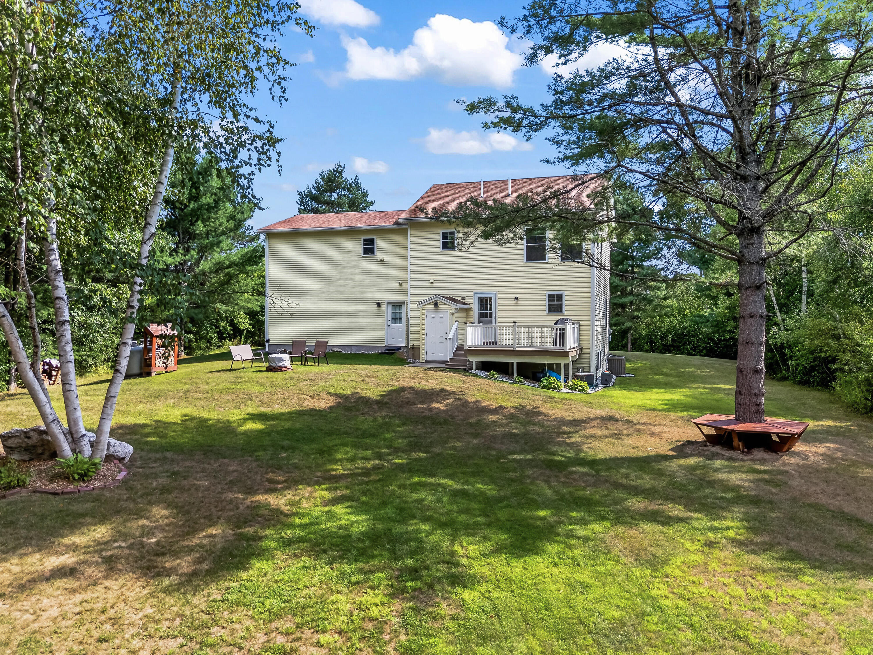 Two-story pale yellow home with a deck in a tree-shaded backyard.