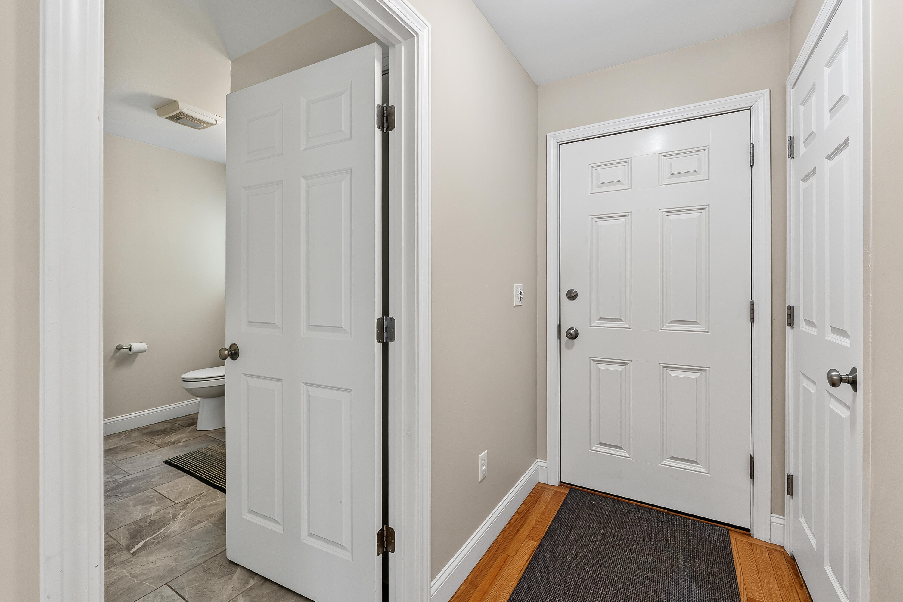 Entry hall with a white paneled front door, hardwood floors, and an adjoining tiled bathroom.