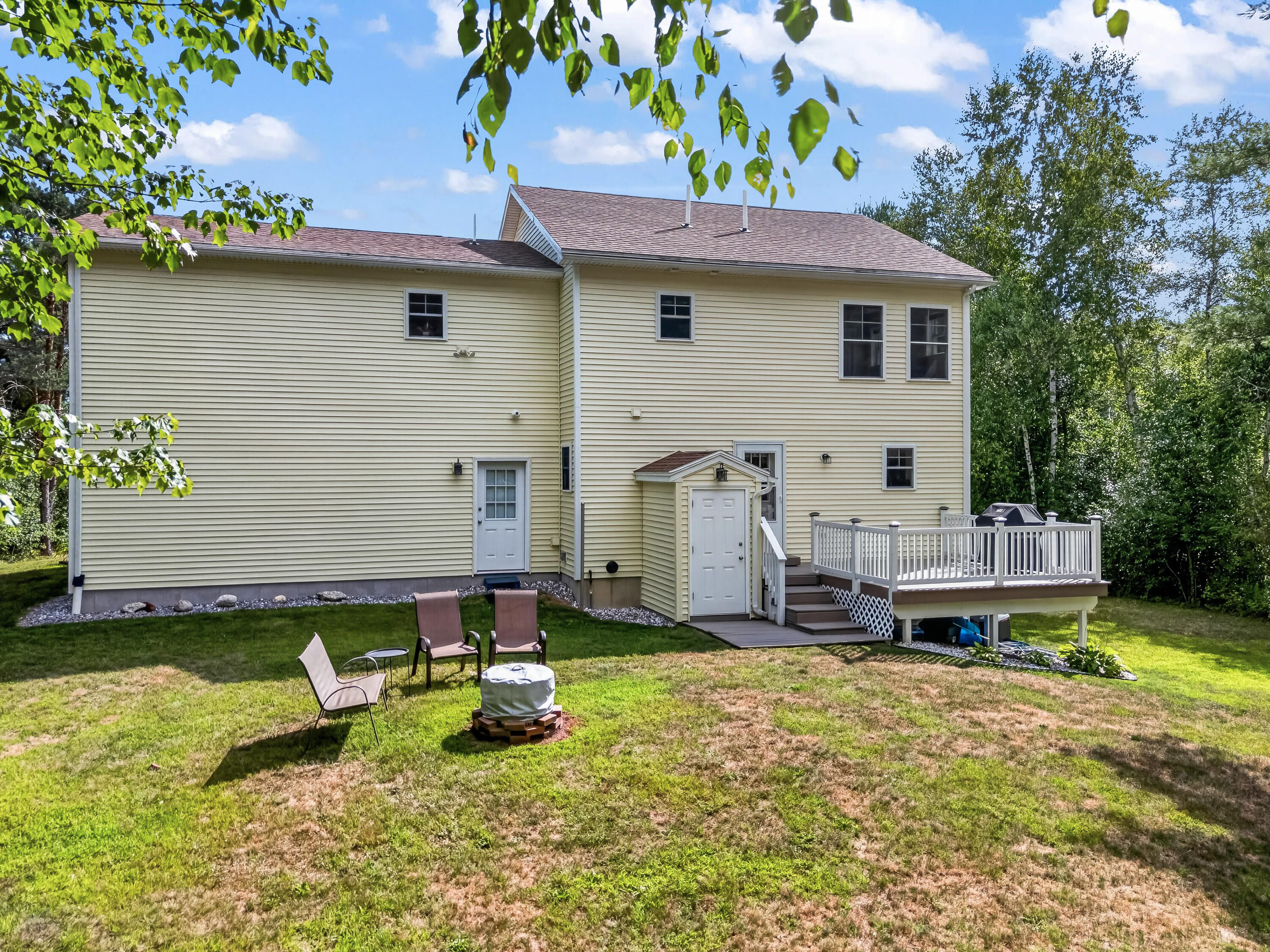 Rear of a pale yellow two-story house with a raised white deck and chairs on the lawn.