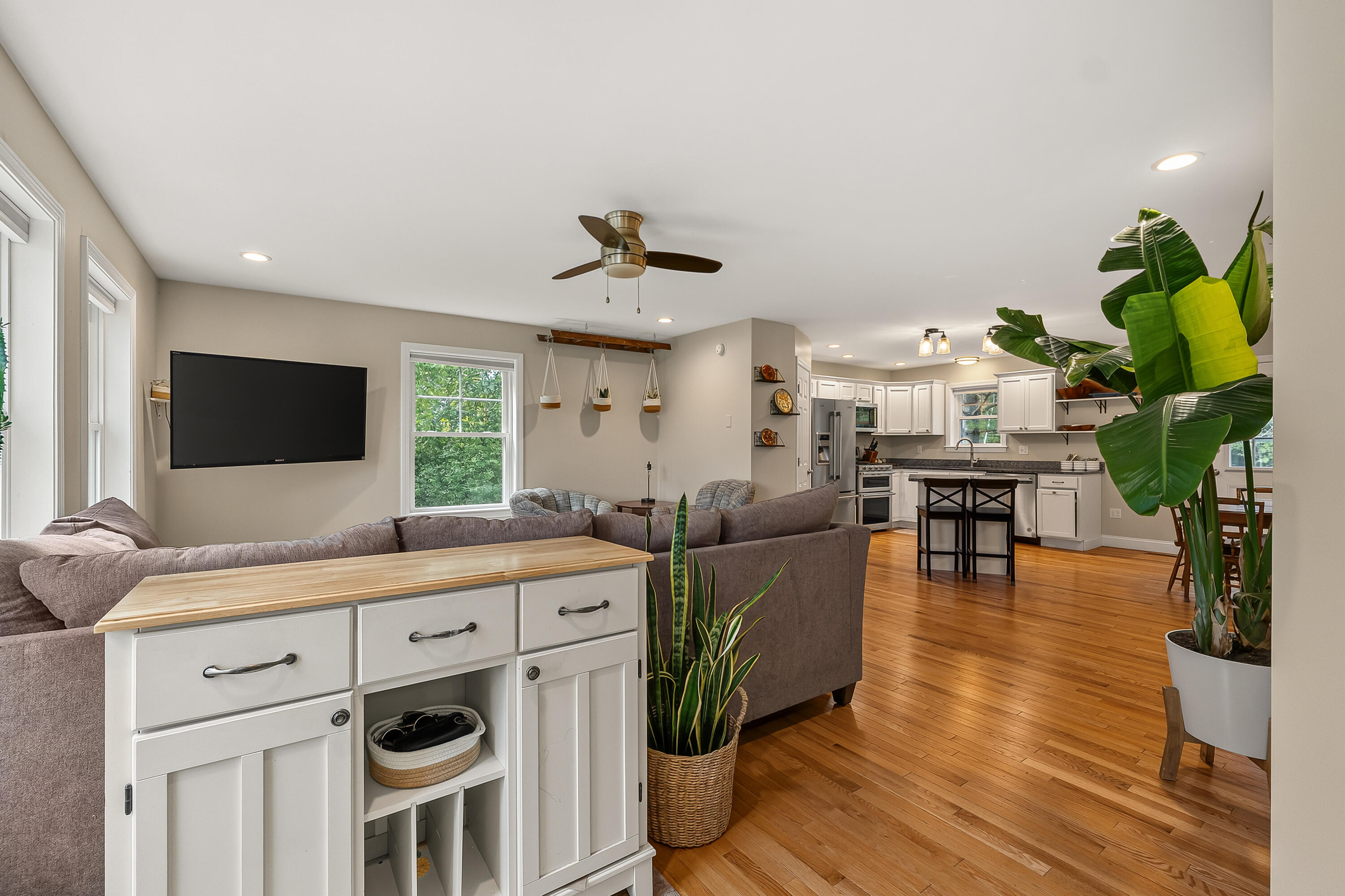 Open-plan living room and kitchen with hardwood floors, gray sectional, white cabinets, and a kitchen island.
