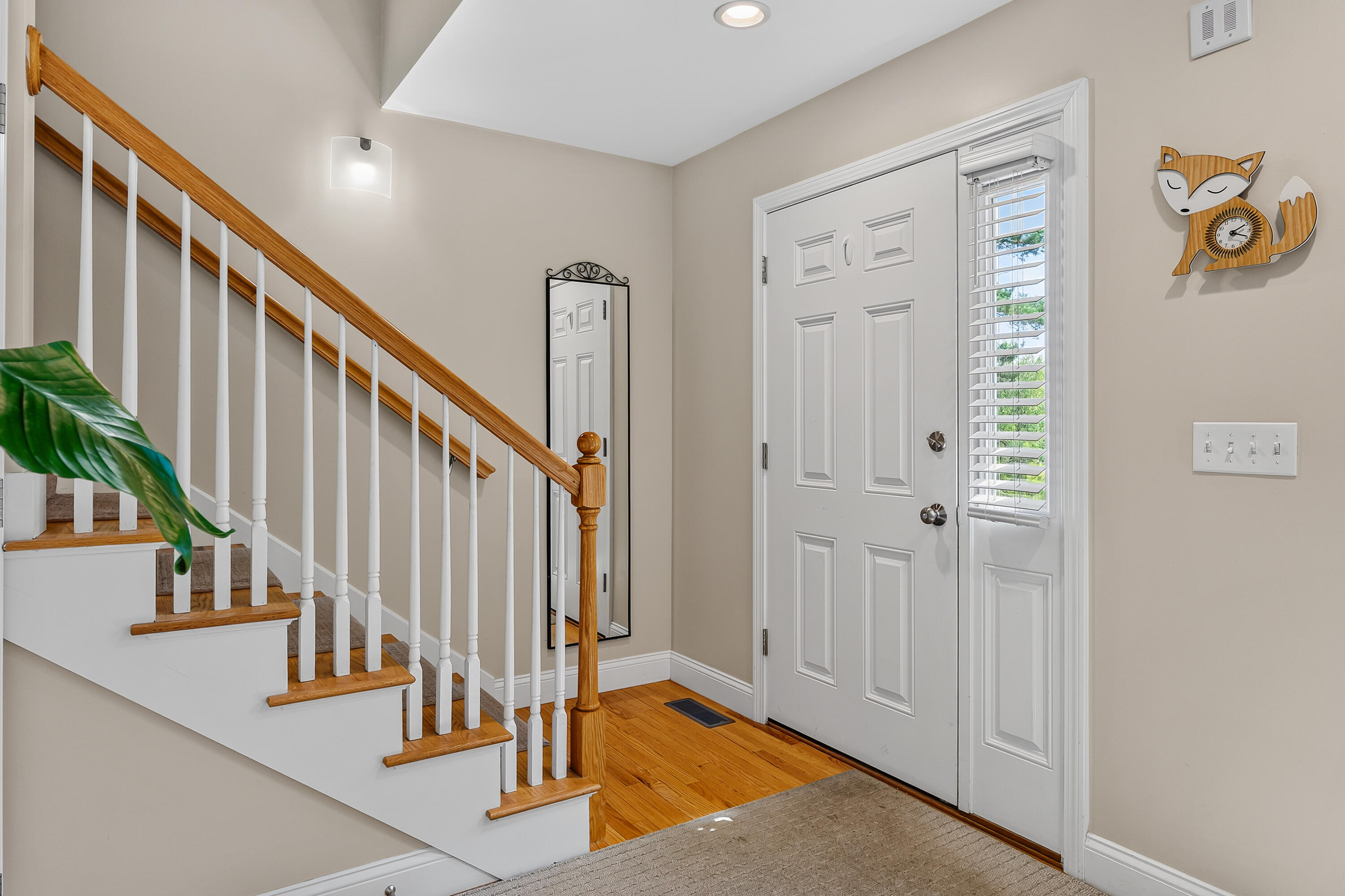 Entry foyer with a white front door, narrow sidelight, and staircase with warm wood treads and handrail.