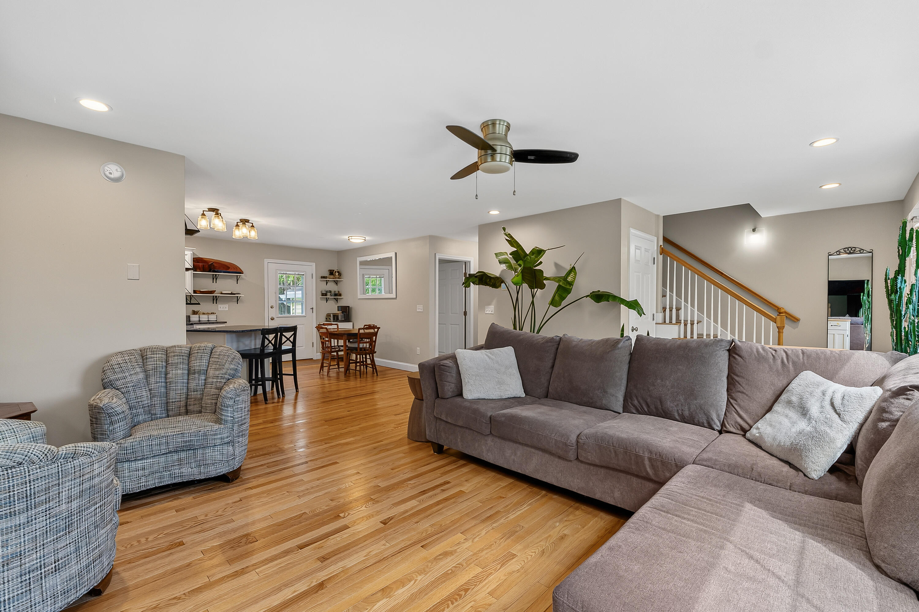 Open-plan living room with hardwood floors, a large sectional, patterned armchairs, and dining area.