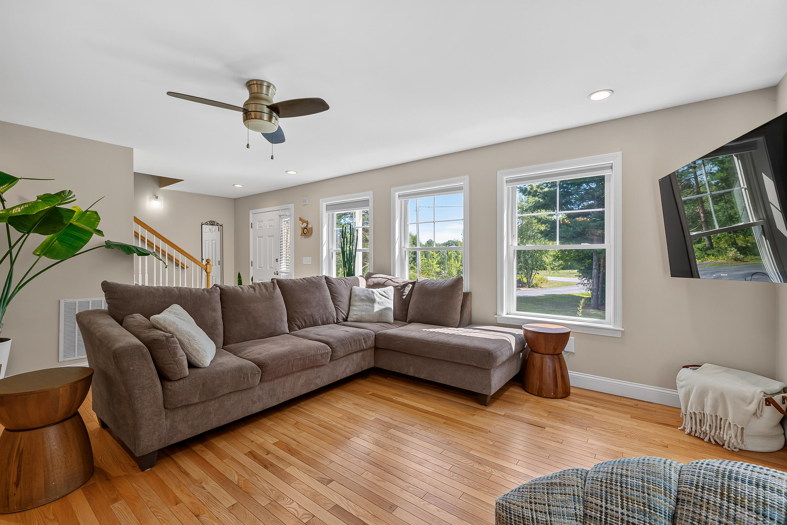 Living room with a brown sectional, hardwood floors, and large windows overlooking trees.