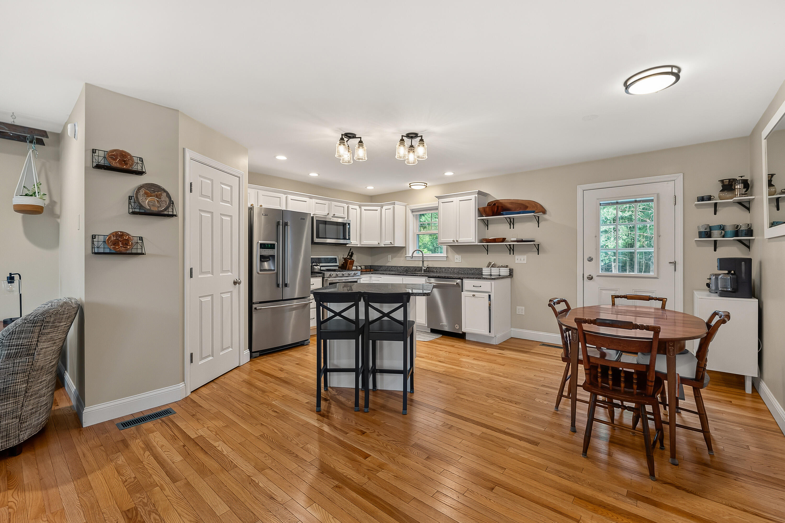 Kitchen and dining area with white cabinets, stainless steel appliances, a central island, and hardwood floors.