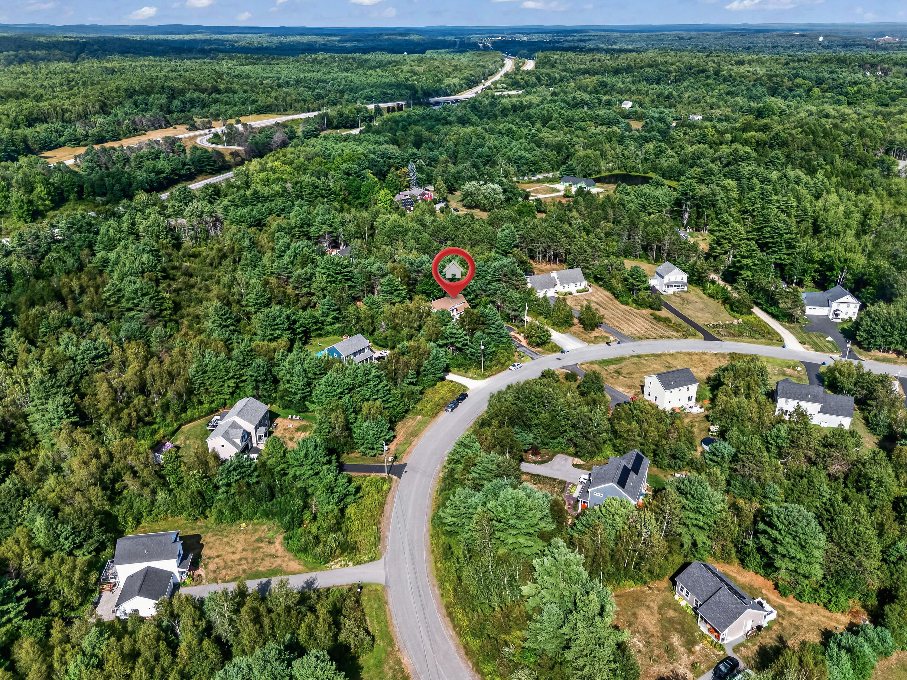Aerial view of wooded homes and winding roads, with a pin marking the property.
