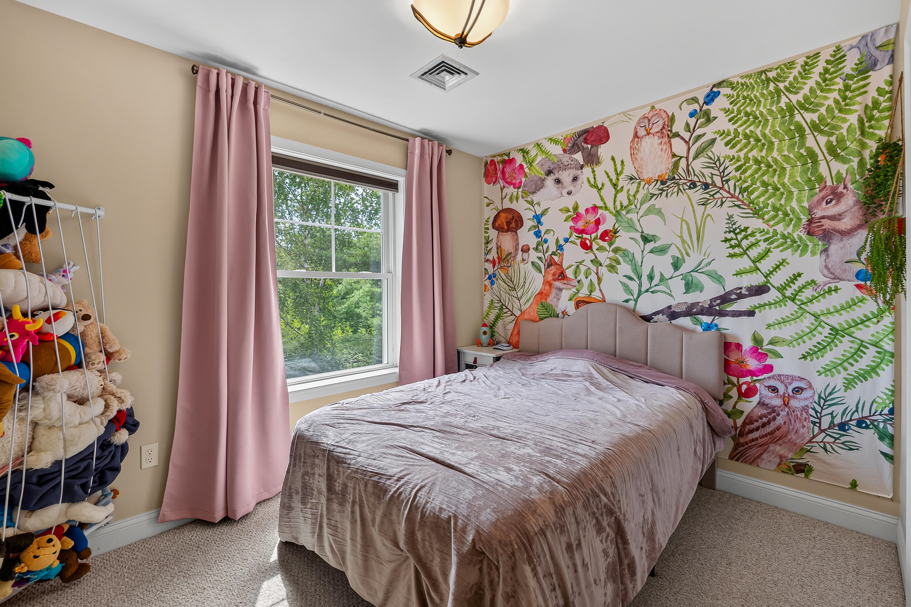 Bedroom with a woodland animal mural, pink curtains, and a bed beneath the mural.