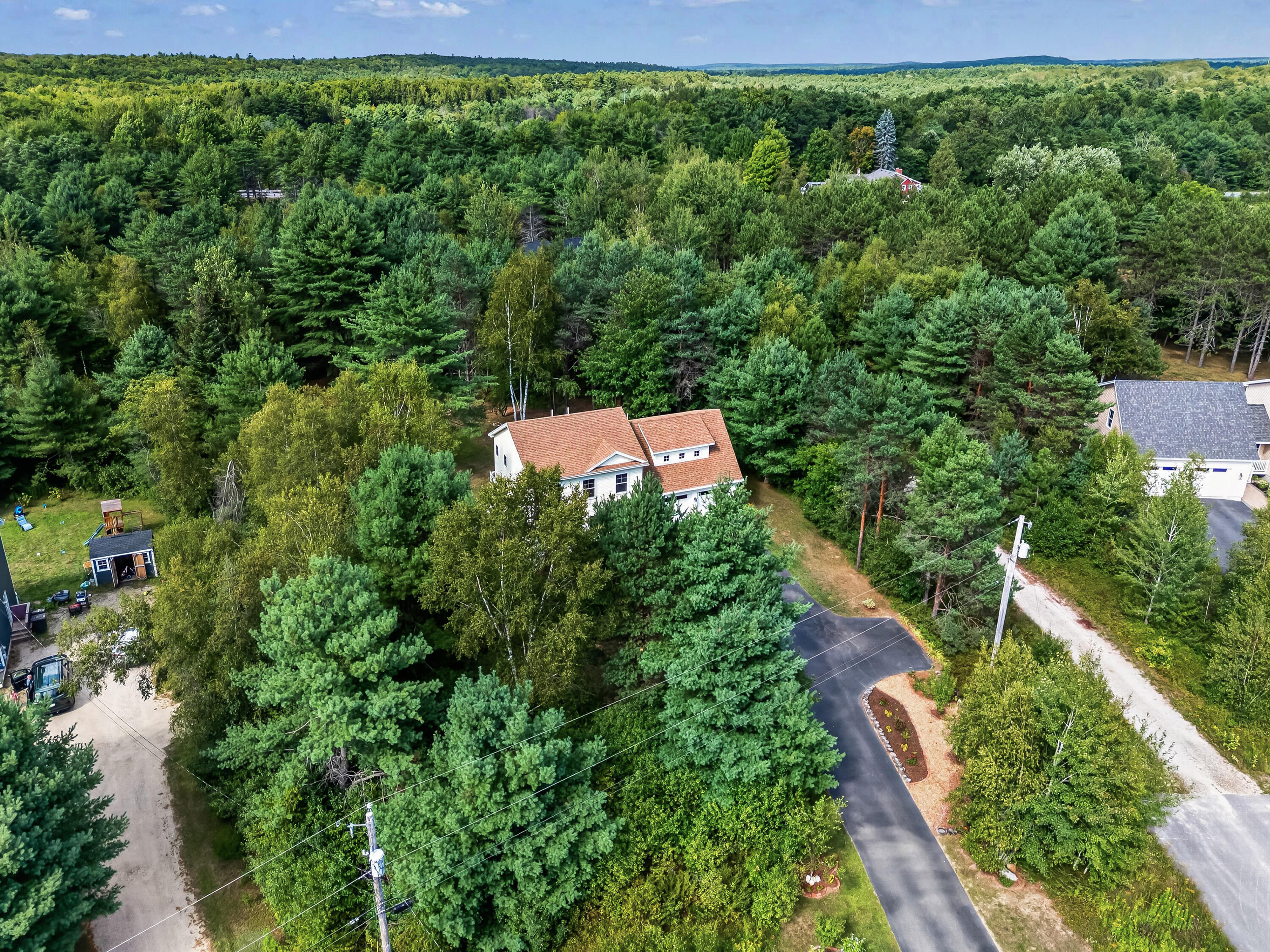 Aerial view of a white, terracotta-roofed house surrounded by dense woodland and a paved driveway.