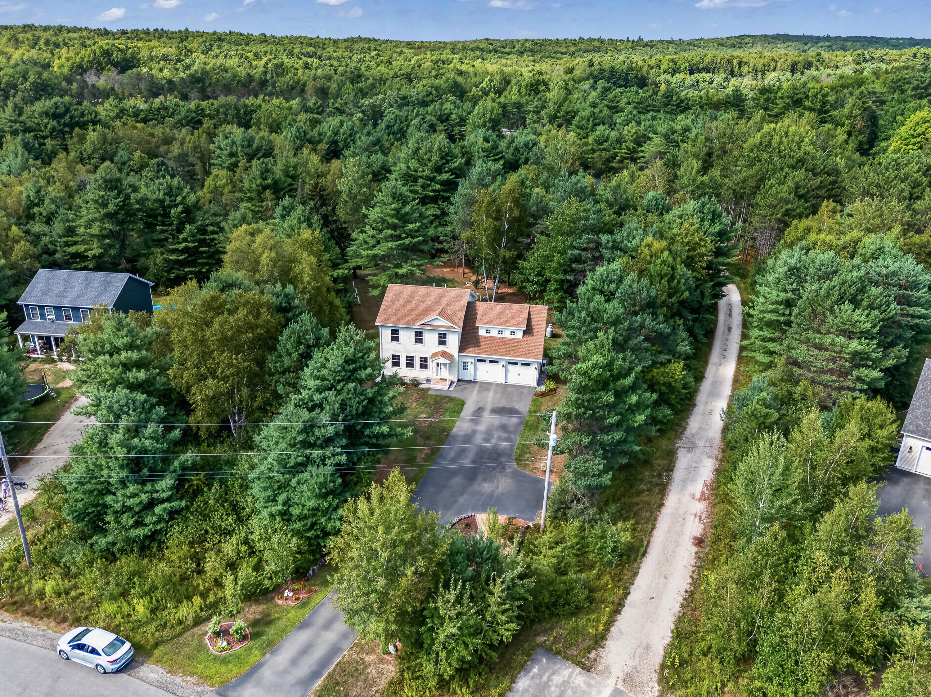 Aerial view of a white house and driveway surrounded by dense woods beside a gravel road.