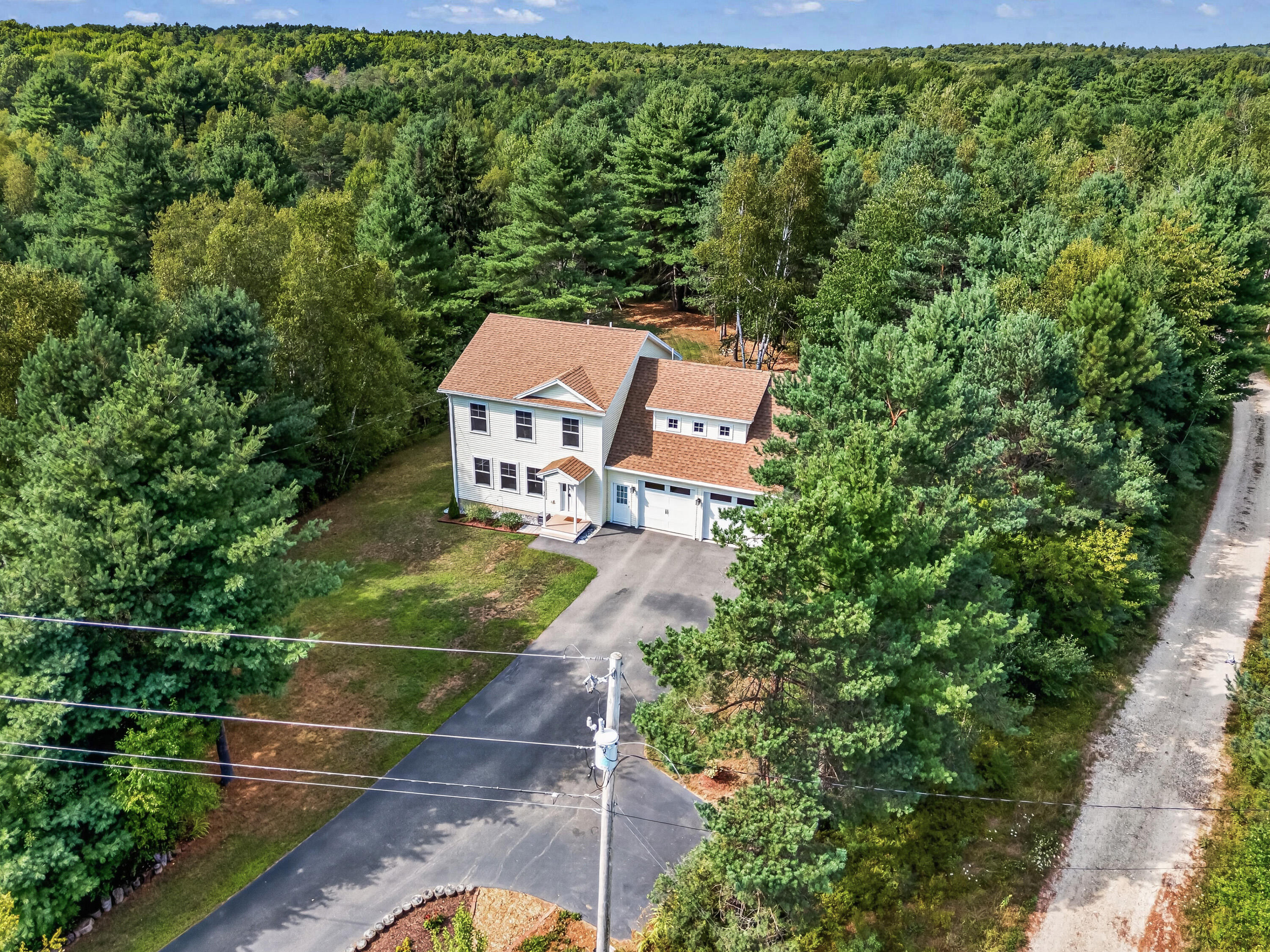 Aerial view of a white two-story house with an attached garage, surrounded by dense trees.