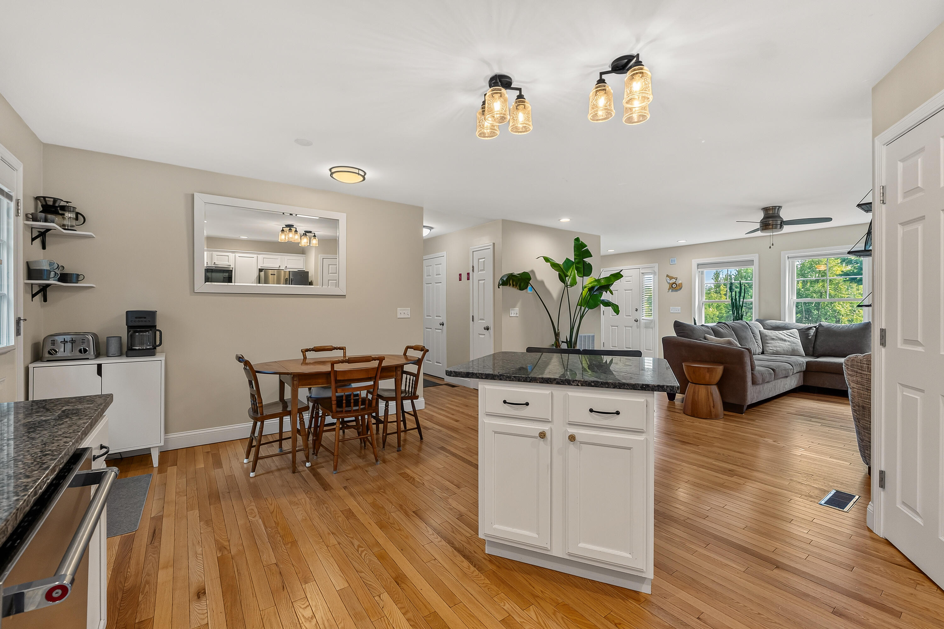 Open-plan kitchen and living area with a stone-topped island, hardwood floors, dining table, and gray sectional.