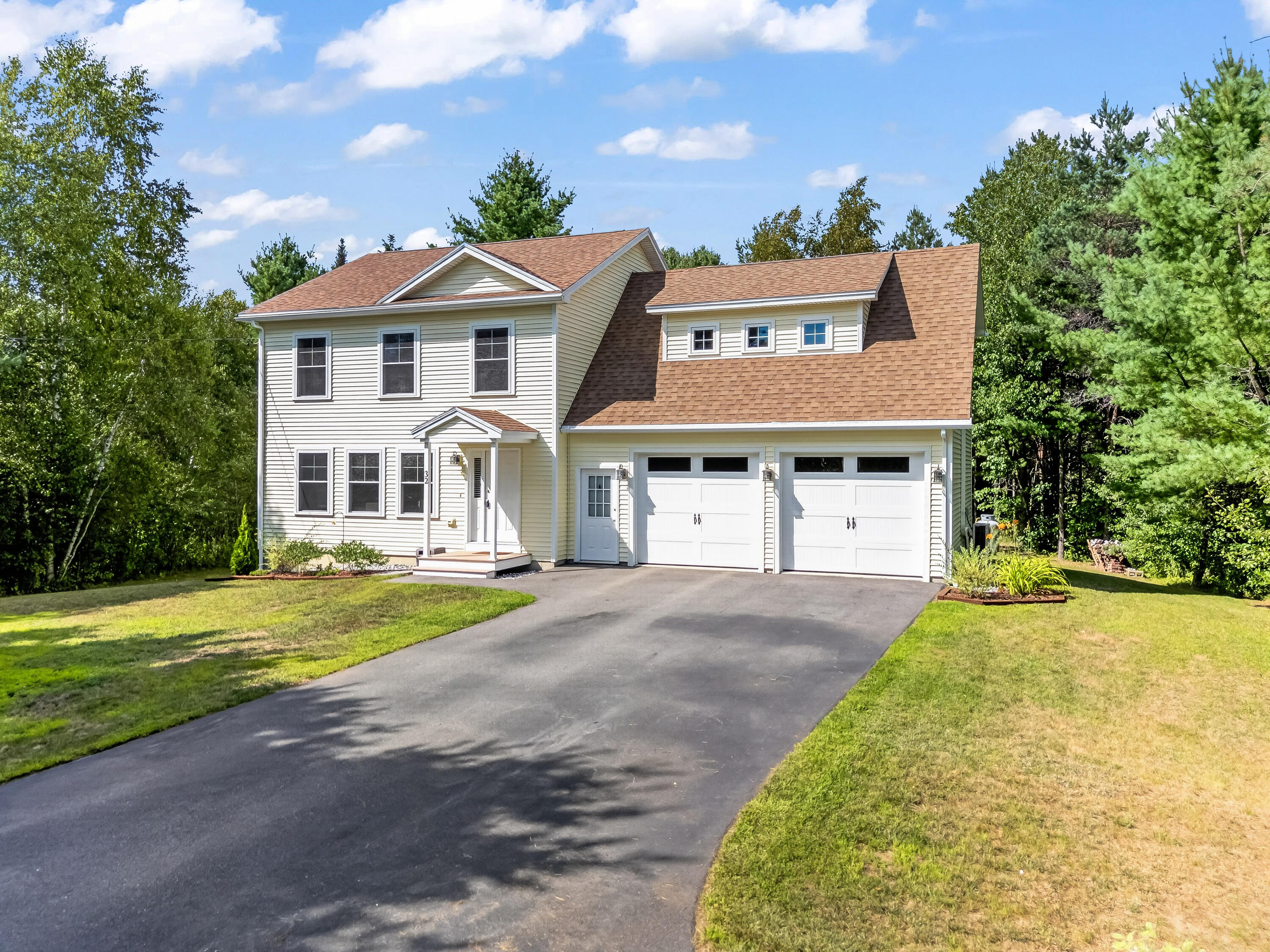 Two-story white house with a brown roof, two-car garage, and wide paved driveway.